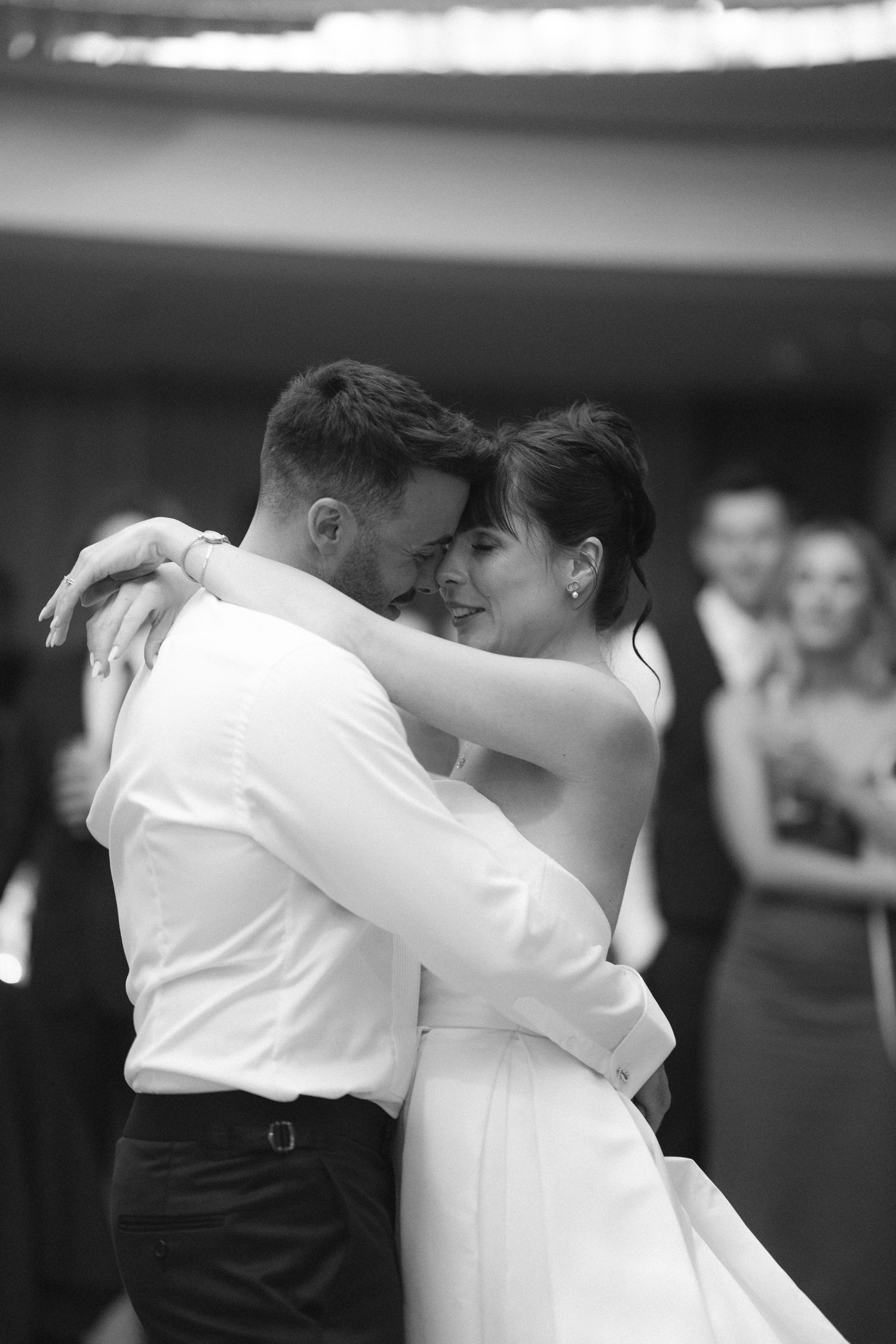 Black and white photo of newlyweds embracing during their first dance at wedding reception.