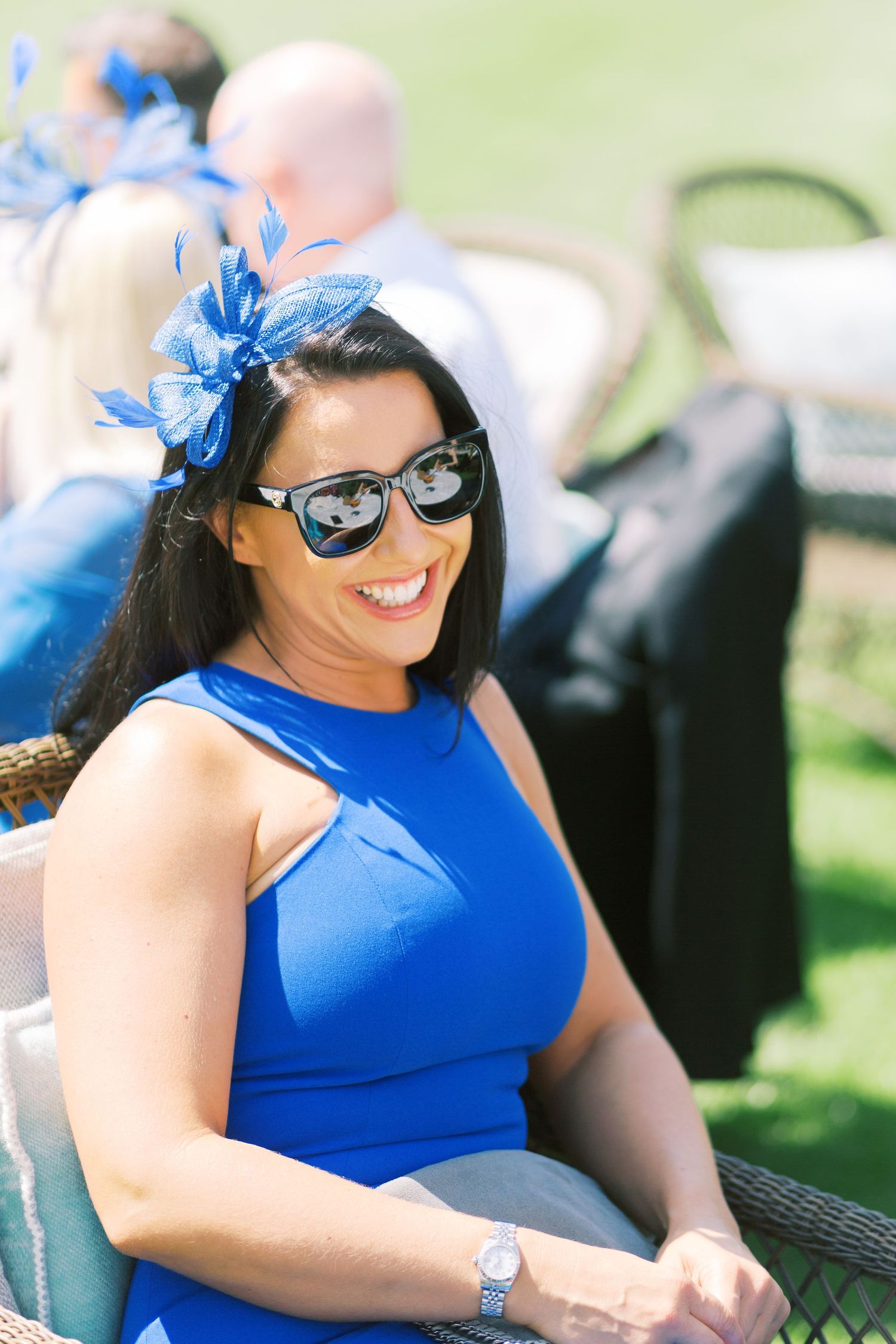 Woman in blue dress and fascinator smiling at outdoor wedding.