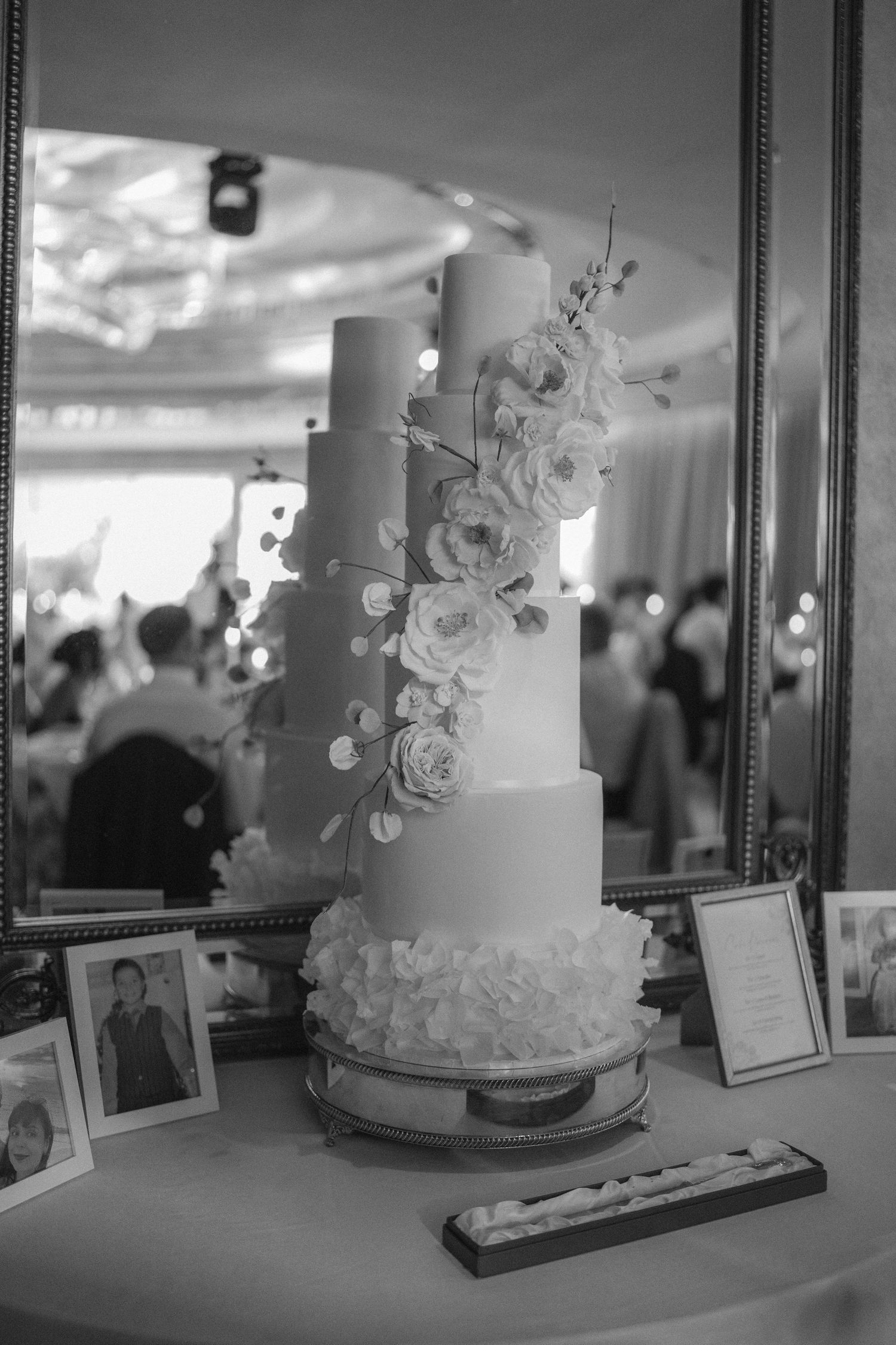 Elegant five-tier white wedding cake adorned with cascading sugar flowers displayed on a table in a reception venue.