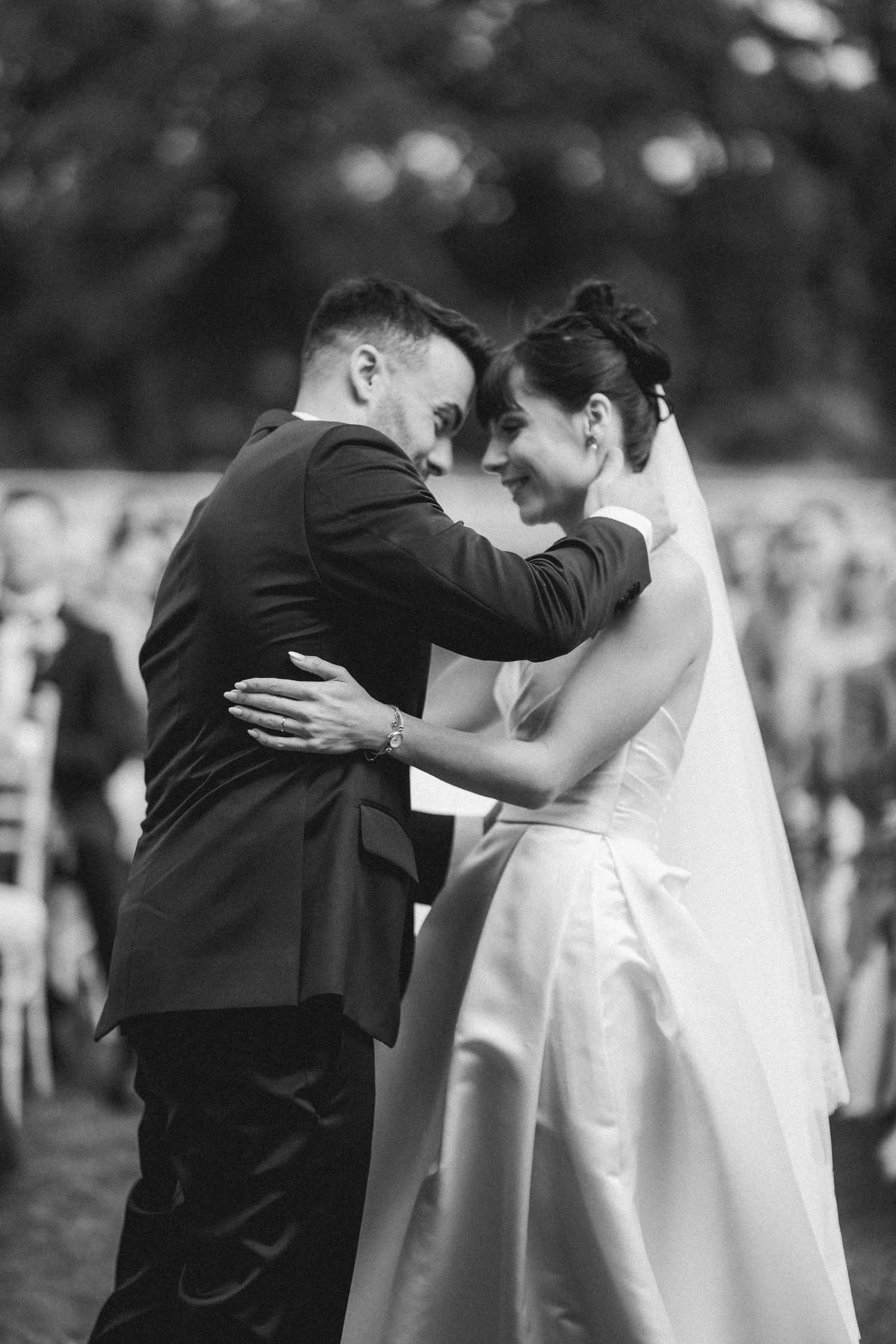 Bride and groom embracing at outdoor wedding ceremony in elegant black and white portrait.