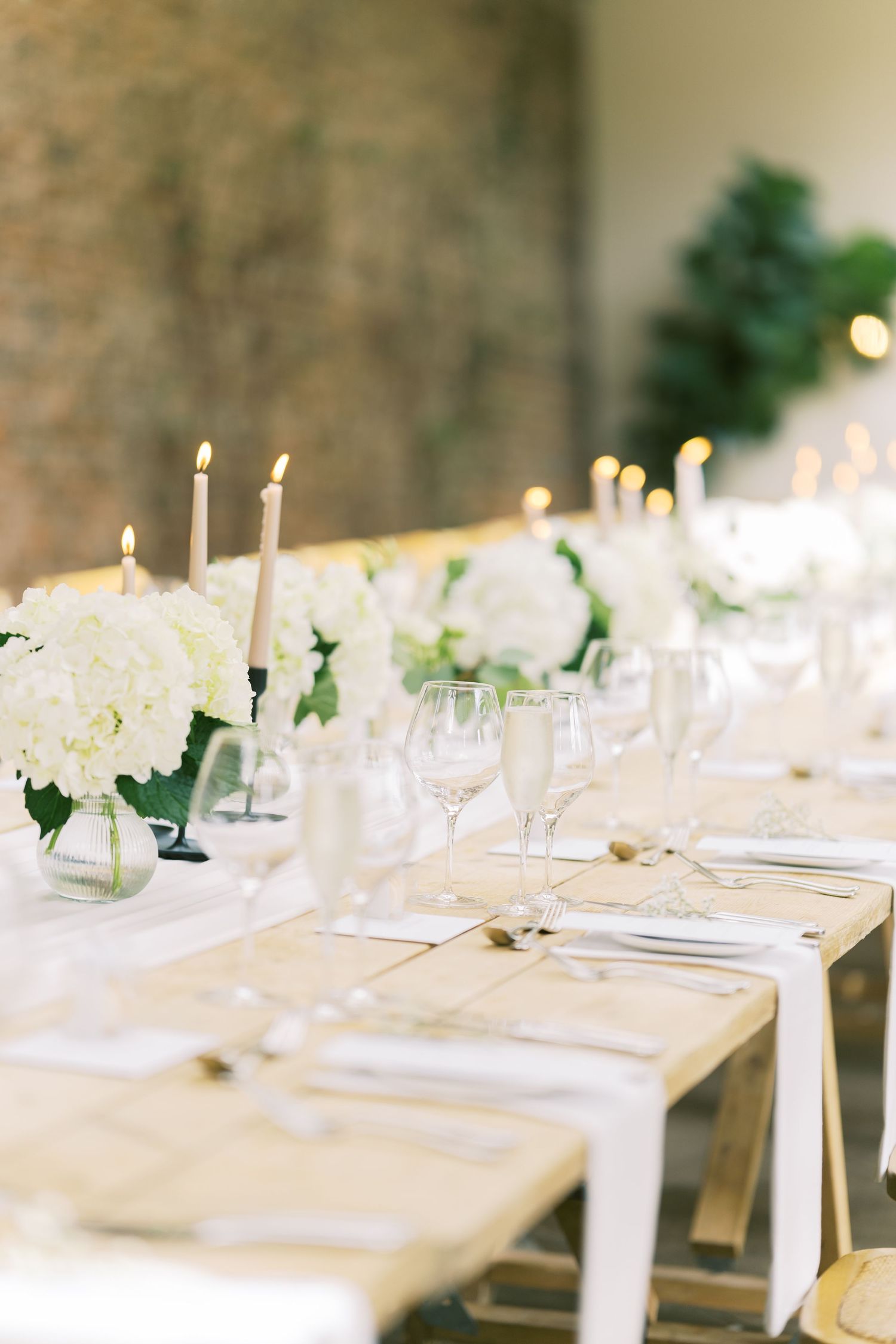 Elegant wedding reception table with white hydrangeas, lit taper candles, and crystal glassware.
