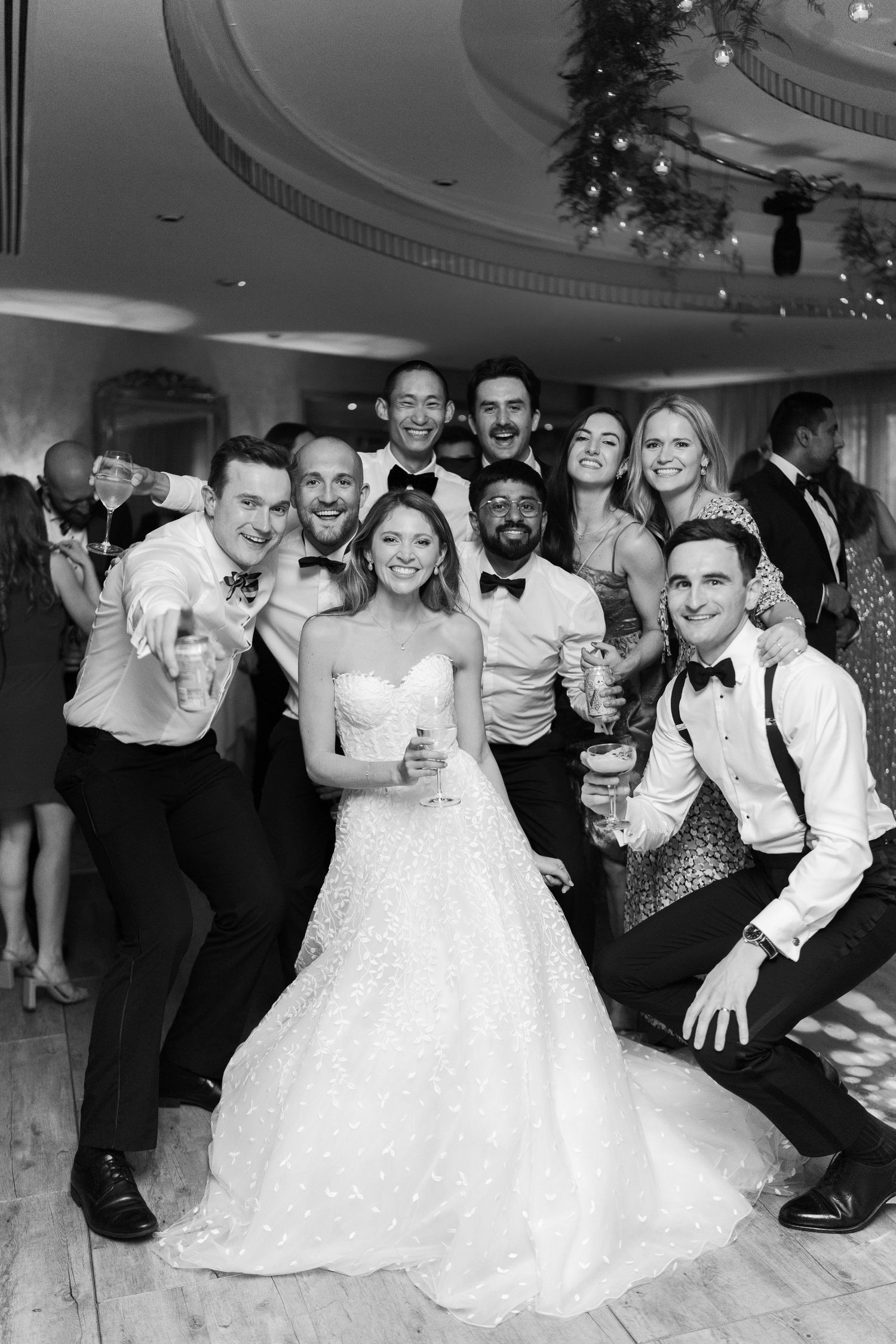 Bride and groom celebrate with friends at wedding reception, posing for a fun black and white group photo.