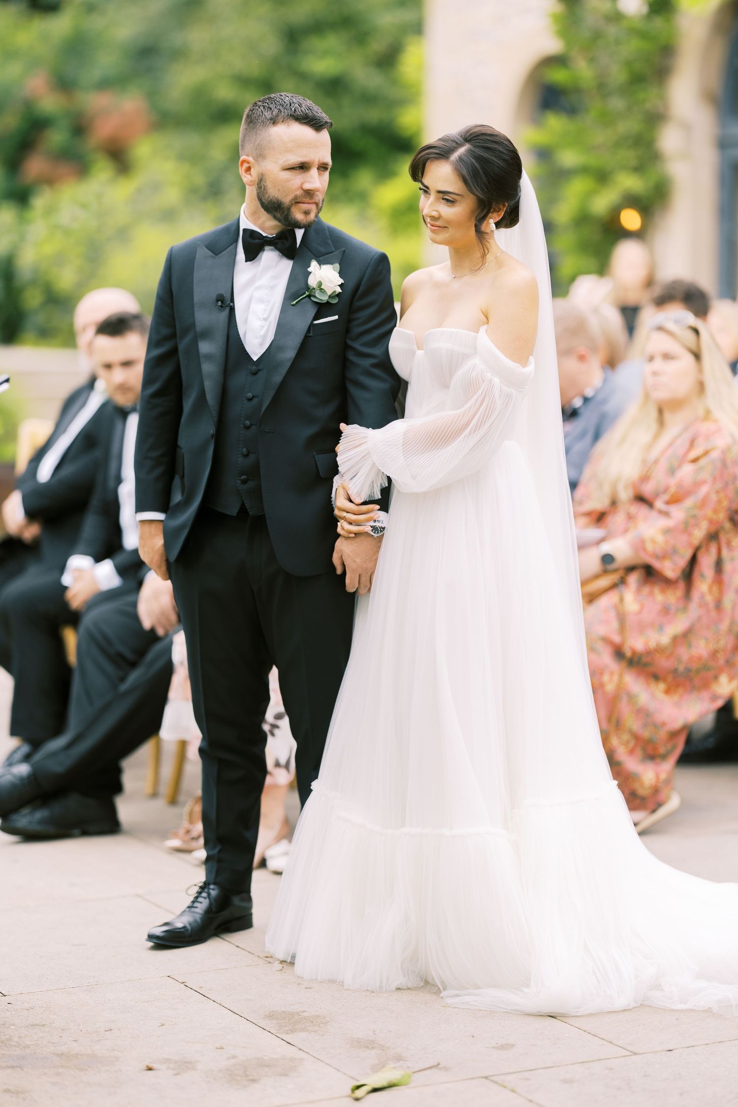 Newlyweds walking arm in arm after outdoor wedding ceremony, bride in elegant white gown and groom in black tuxedo.