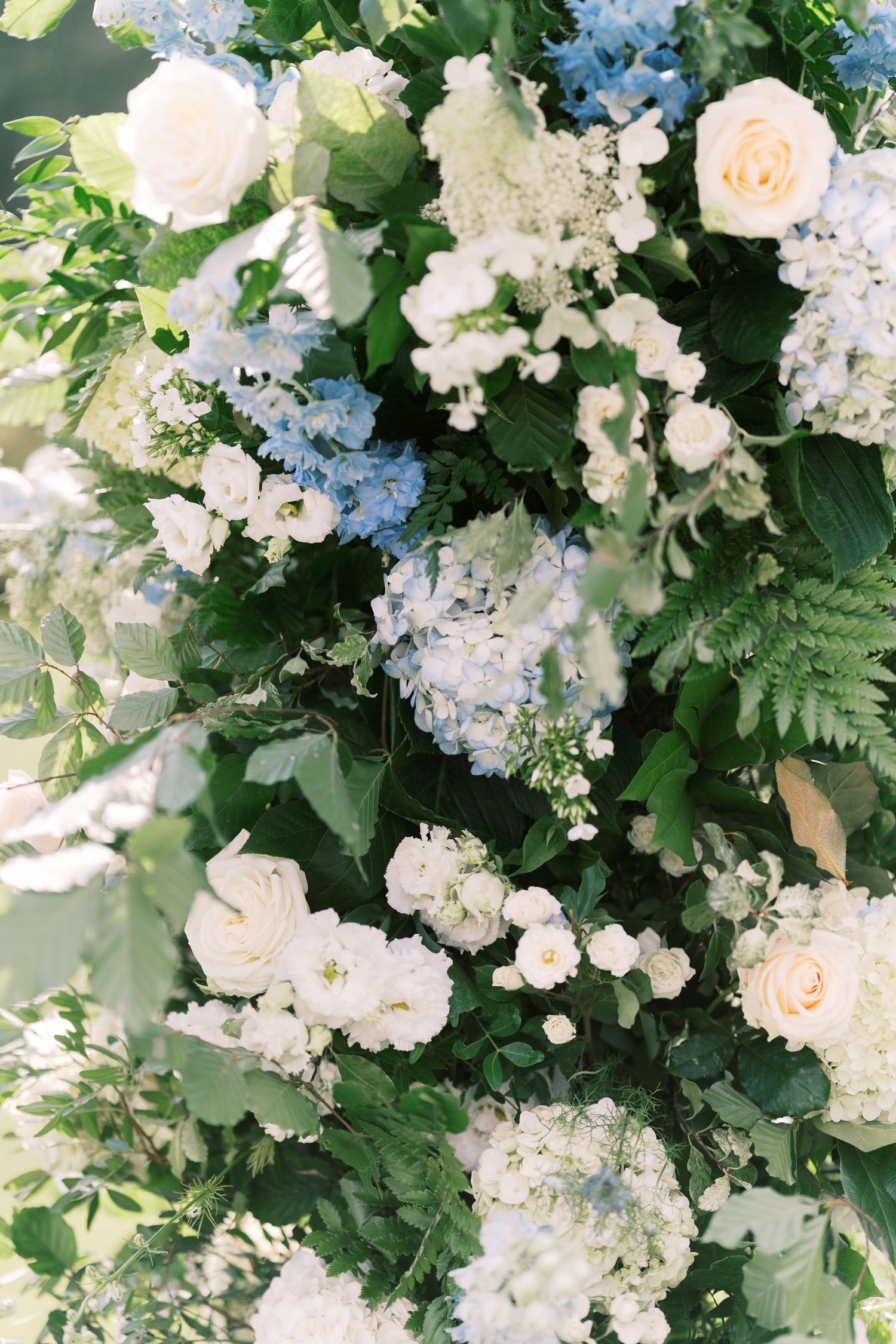 Lush wedding floral arrangement with white roses, blue hydrangeas, and green foliage for an elegant ceremony backdrop.