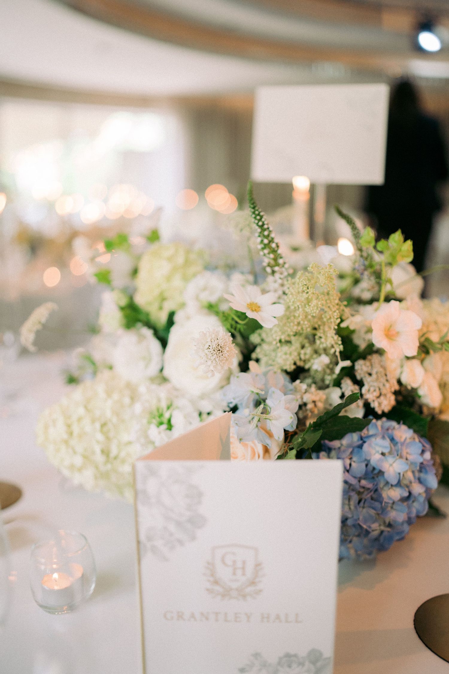 Elegant wedding table centerpiece with white and blue hydrangeas, roses, and a Grantley Hall menu card.