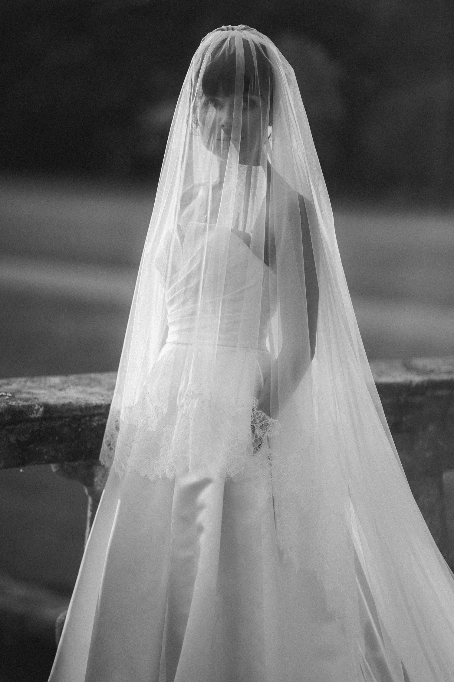 Black and white photo of bride in strapless wedding gown with long flowing veil draped over her face.