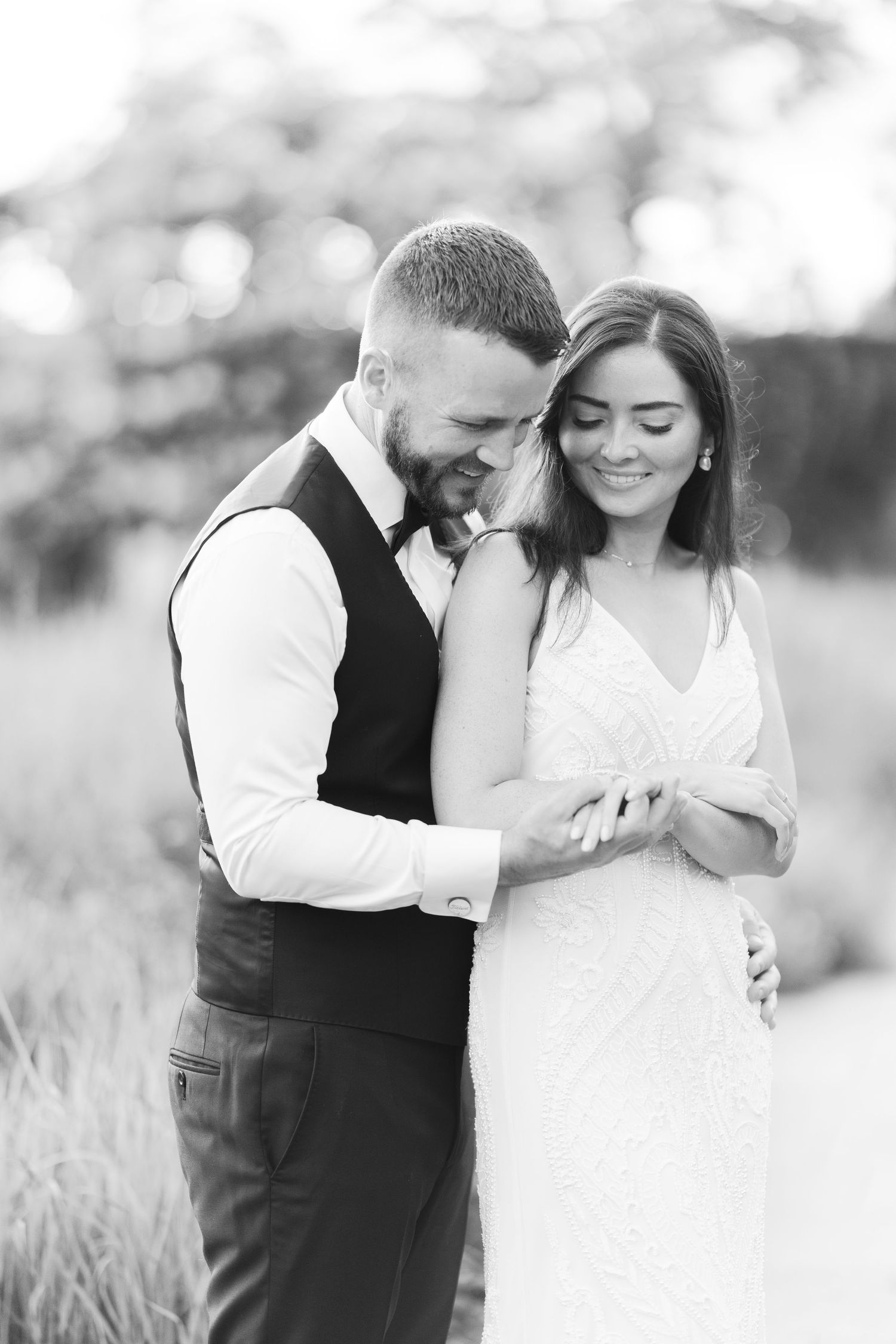 Black and white photo of a groom tenderly embracing his smiling bride in a sunlit garden.