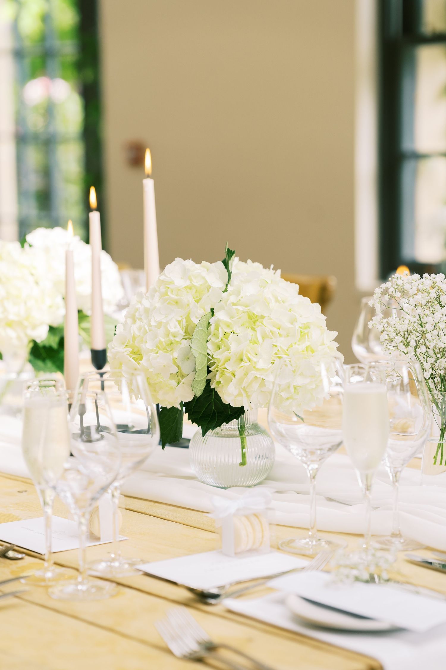 White hydrangea centerpiece with tall taper candles and crystal glassware on elegantly set wedding reception table.