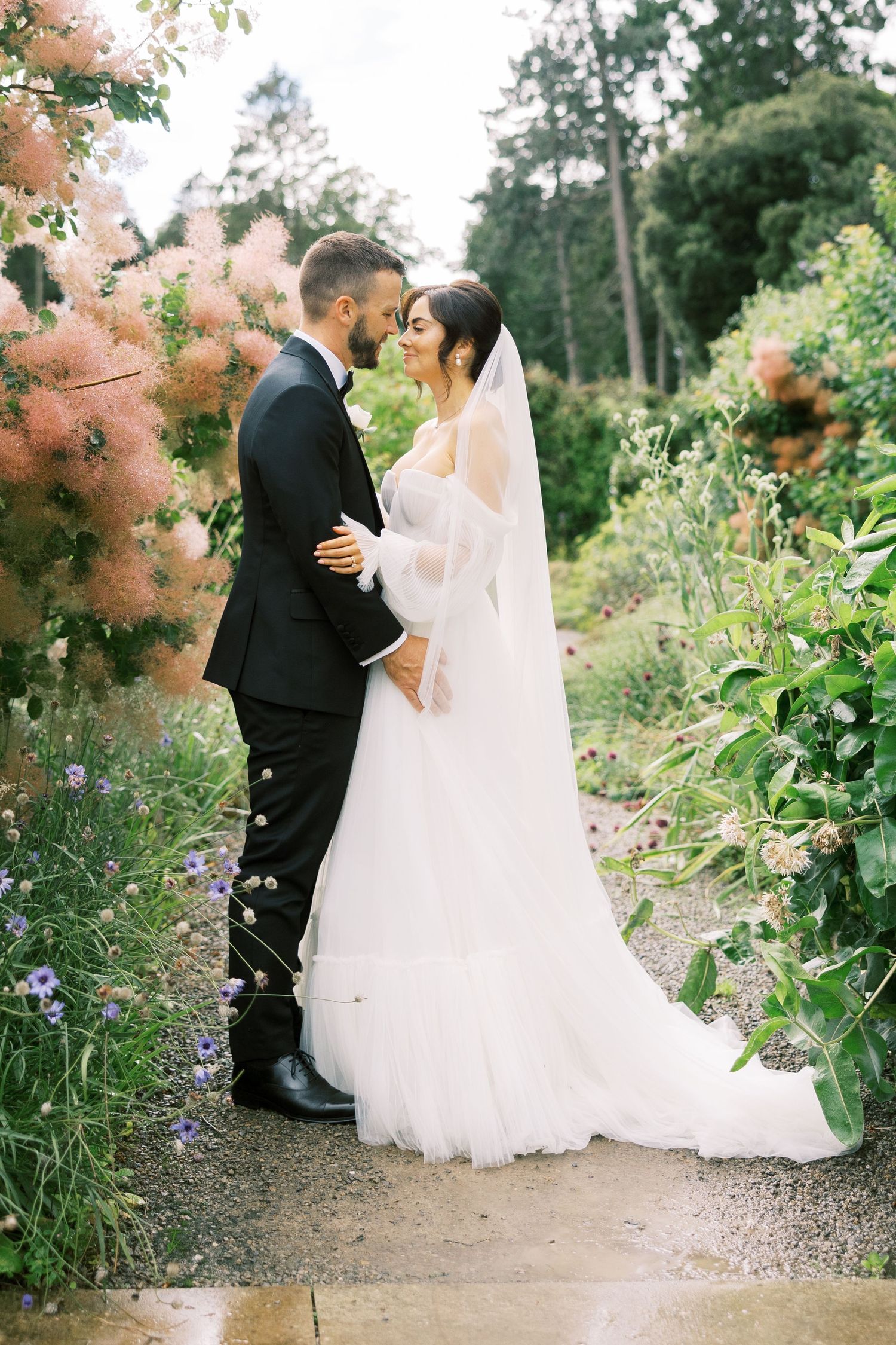 A bride and groom share a romantic moment in a lush garden, with the bride in a white gown and veil.