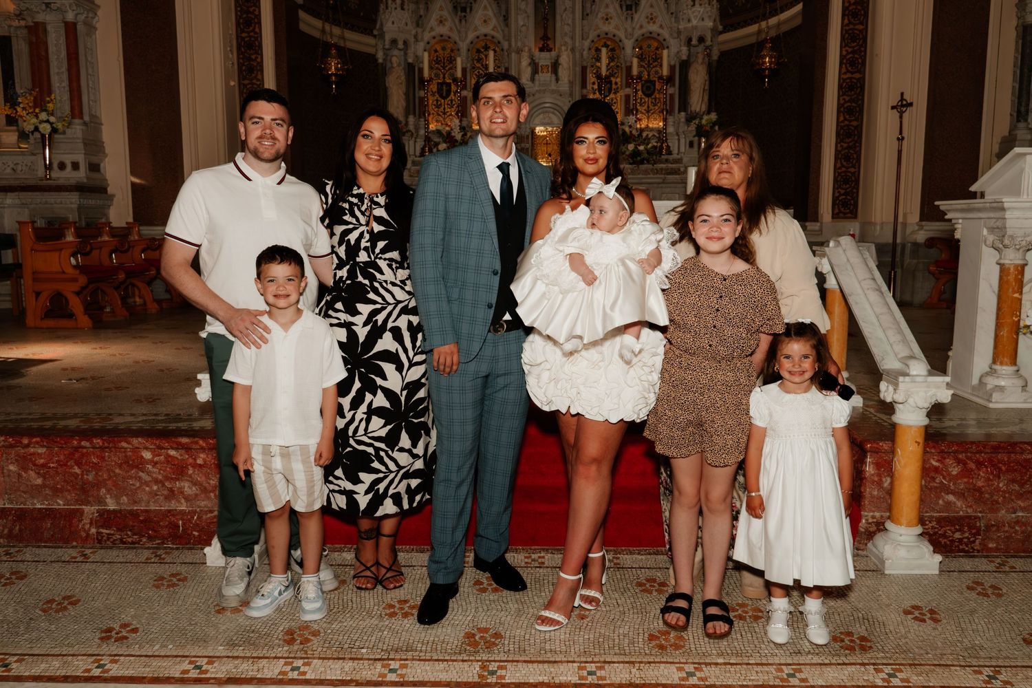Family gathering for a baptism ceremony inside a church, with adults and children posing together near the altar.