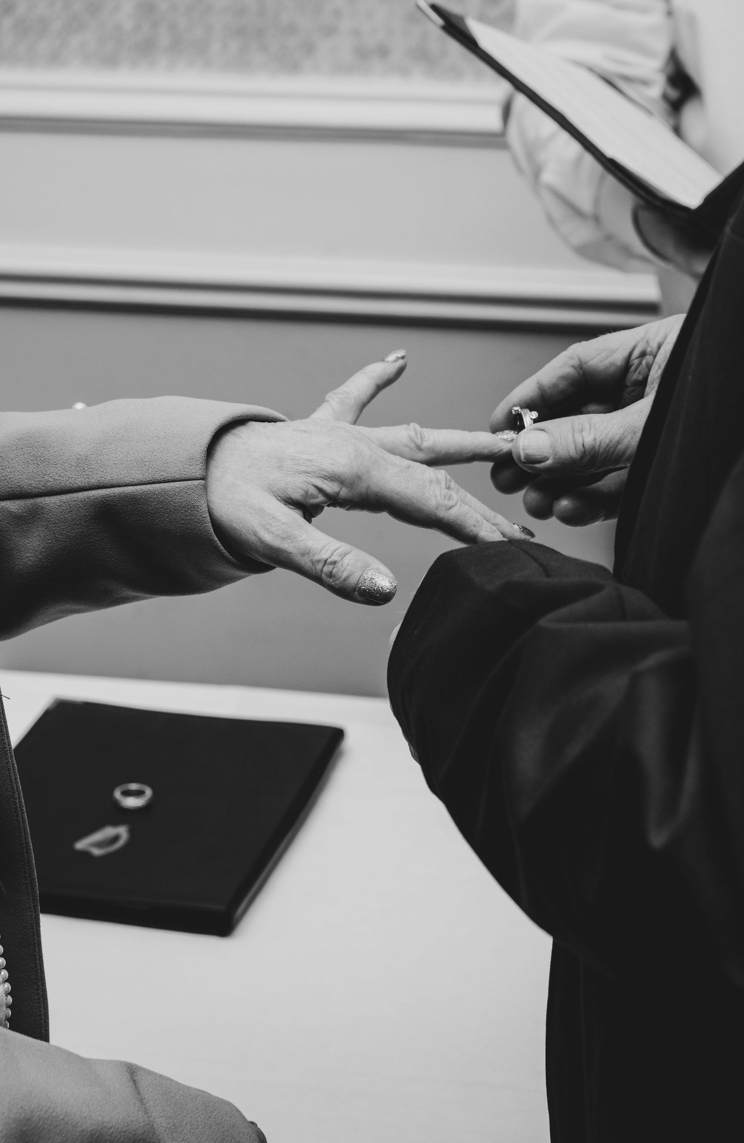 Black and white photo of a officiant placing a wedding ring on a bride's finger during a marriage ceremony.