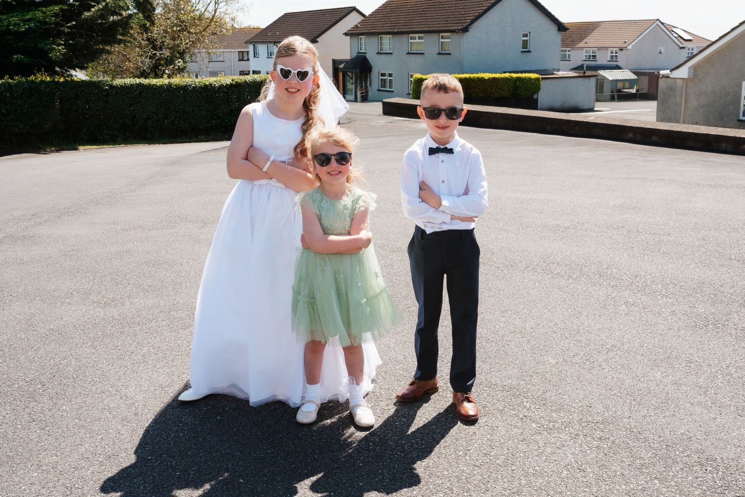 Bride in white dress with two children in sunglasses and formal wear posing outdoors on a sunny day.