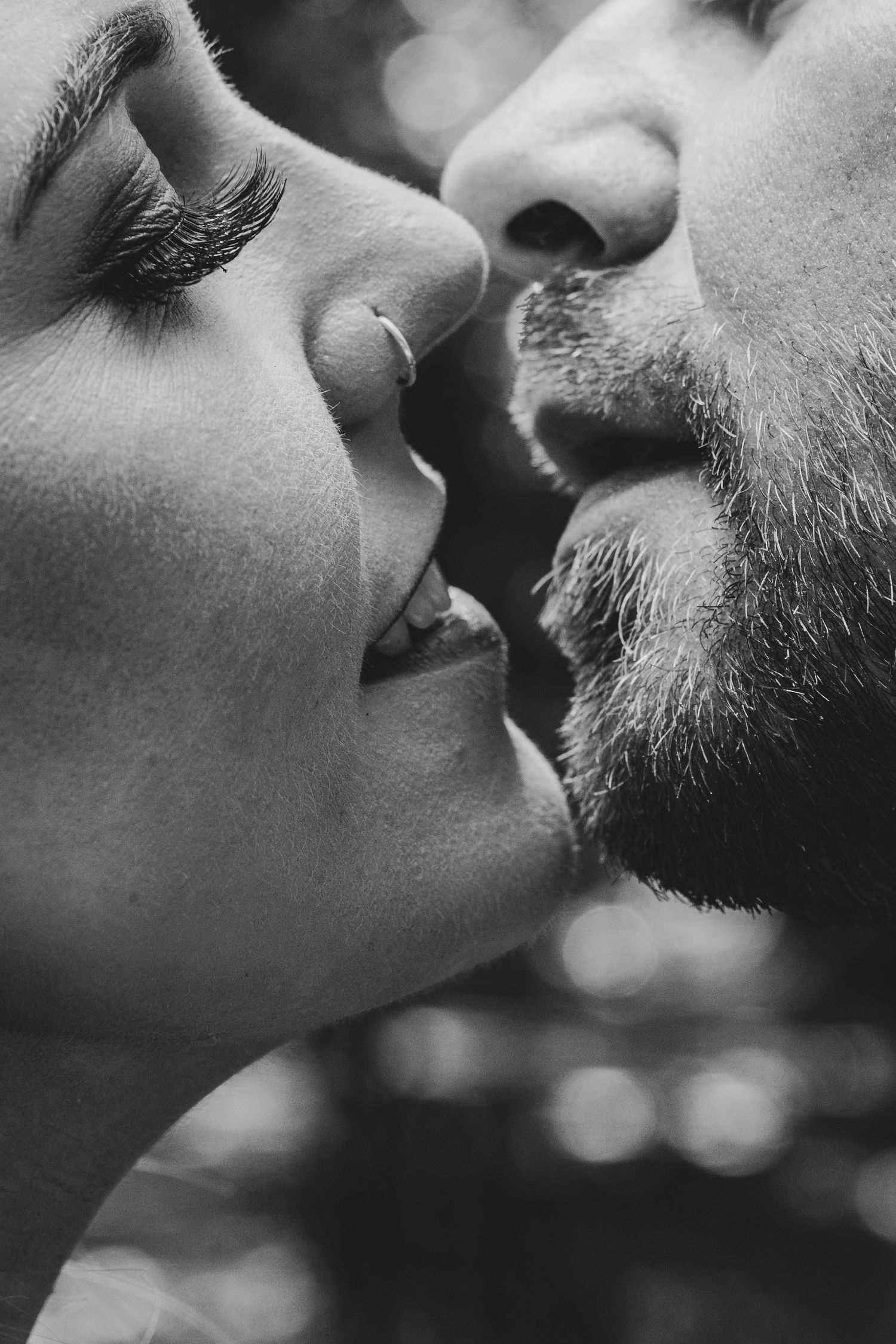 Close-up black and white portrait of a couple sharing a tender kiss, showcasing beard and nose ring.