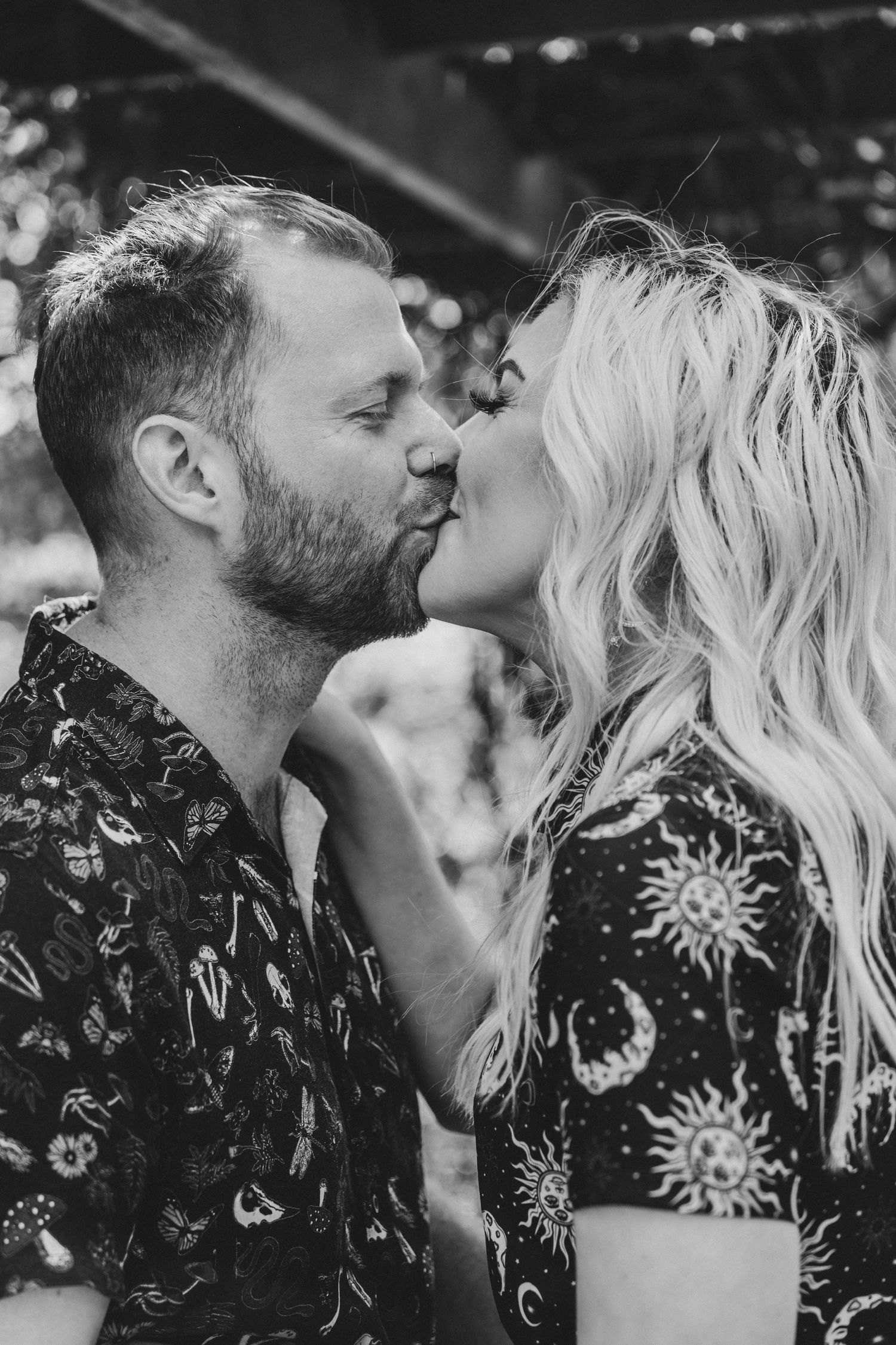 Black and white close-up of a couple sharing a romantic kiss, both wearing celestial patterned clothing.