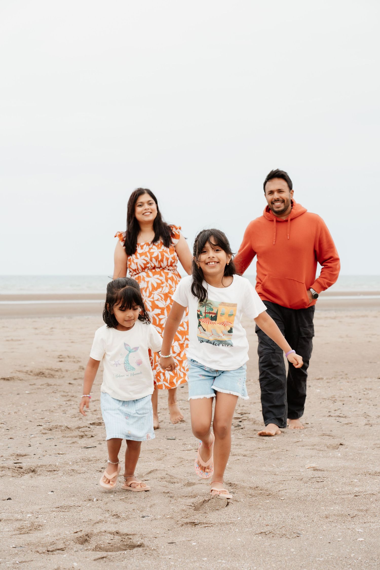 Happy family of four walking together on a sandy beach on a cloudy day.