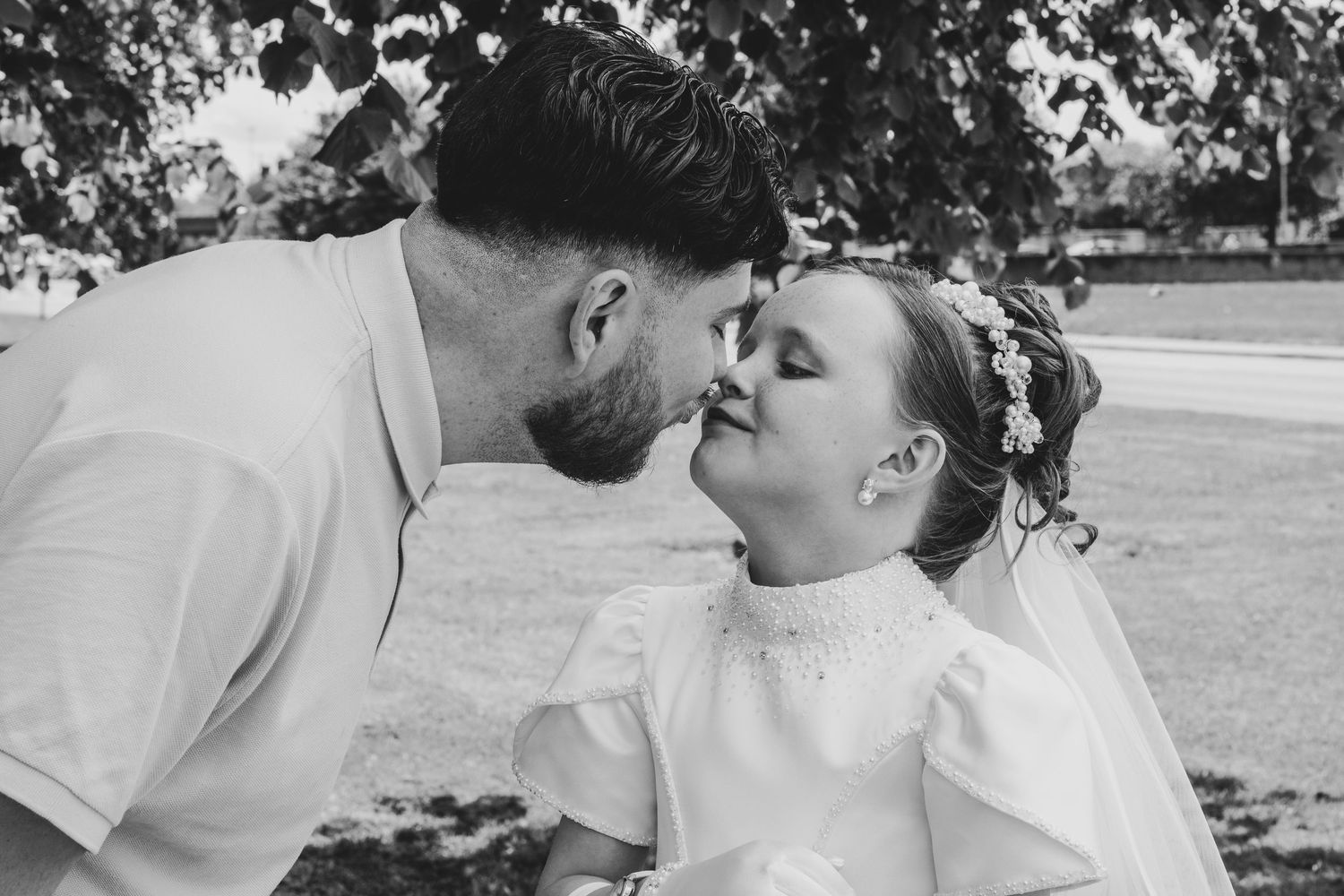 Black and white photo of a man and young flower girl sharing a sweet kiss at a wedding ceremony outdoors.