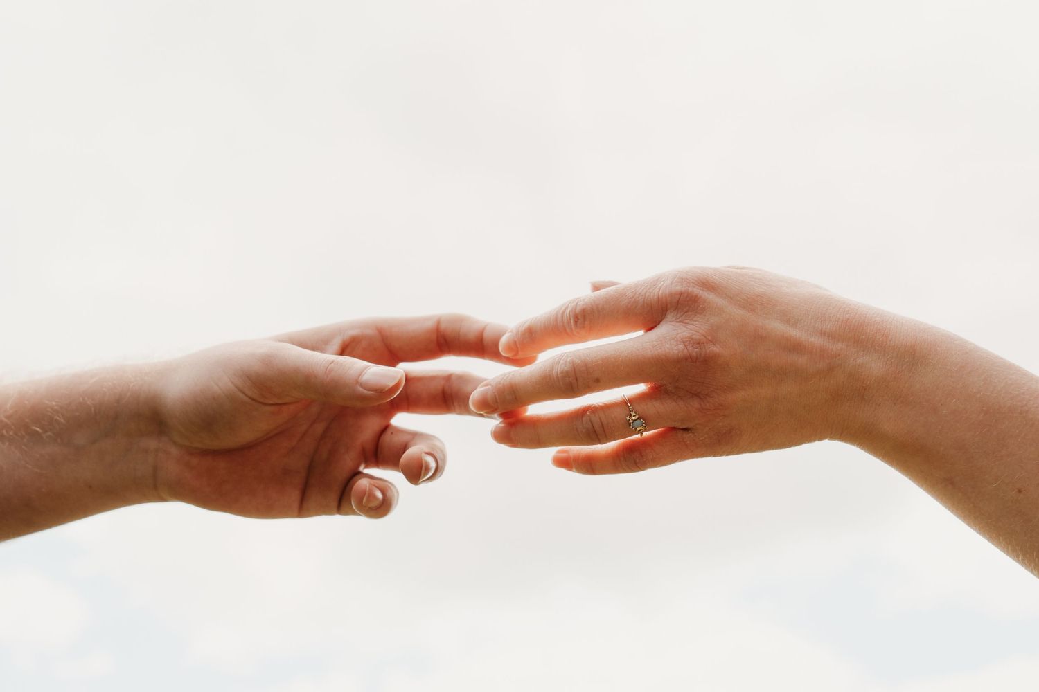 Two hands gently touching fingertips against a soft white background, symbolizing connection and love.