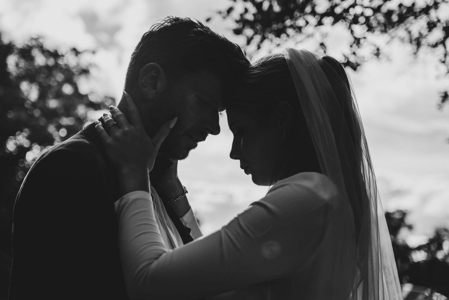 Black and white wedding photo of bride and groom touching foreheads in a romantic intimate moment outdoors.