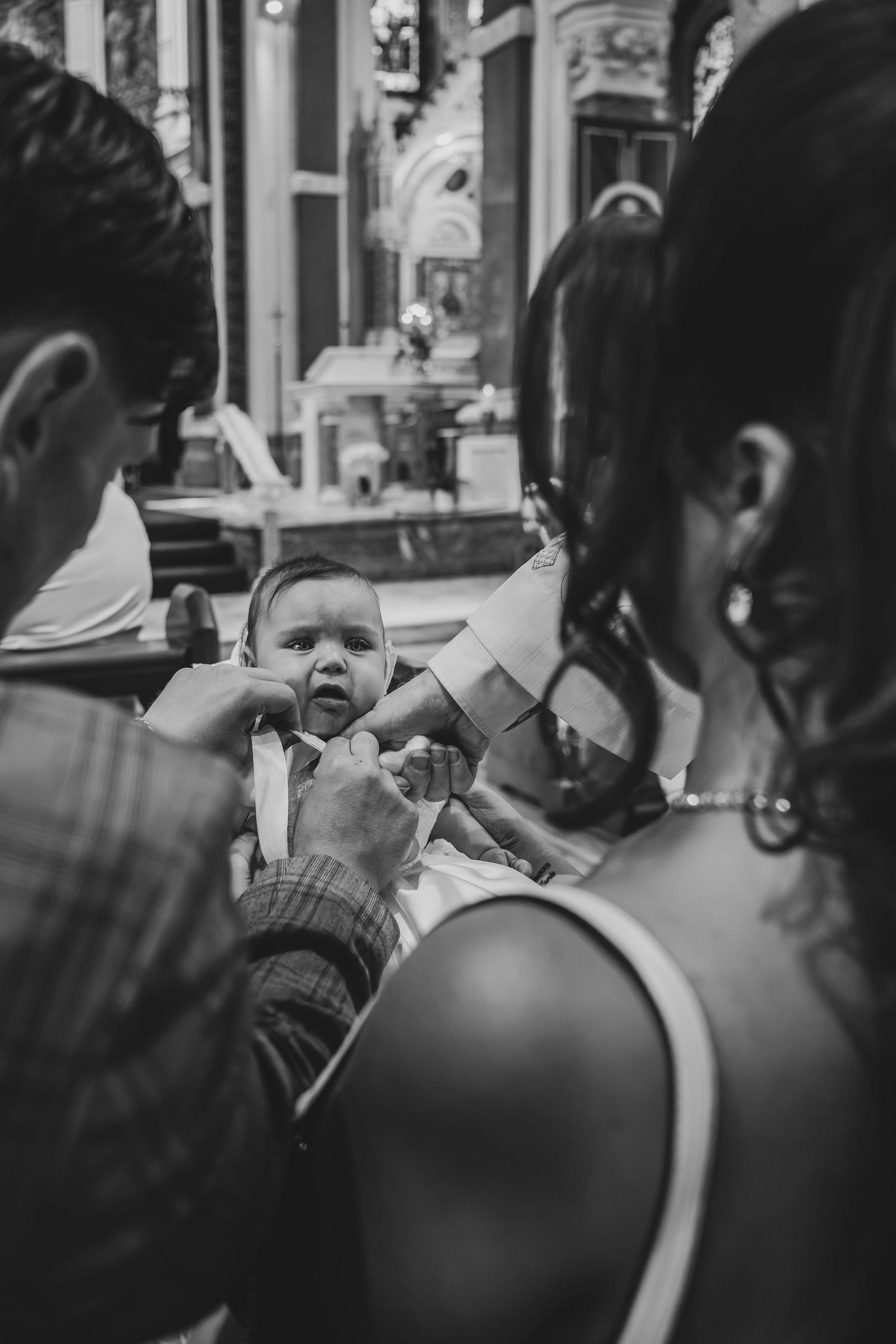 Black and white photo of parents holding their baby during a church baptism ceremony.
