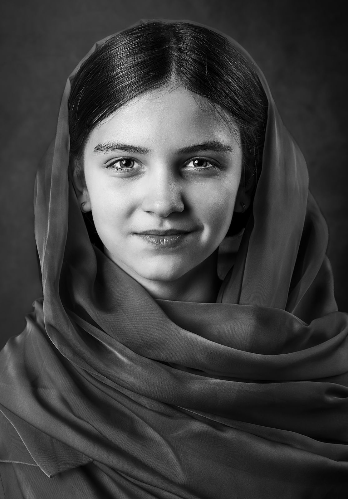 Black and white portrait of a young woman wearing a flowing headscarf, smiling softly at the camera.