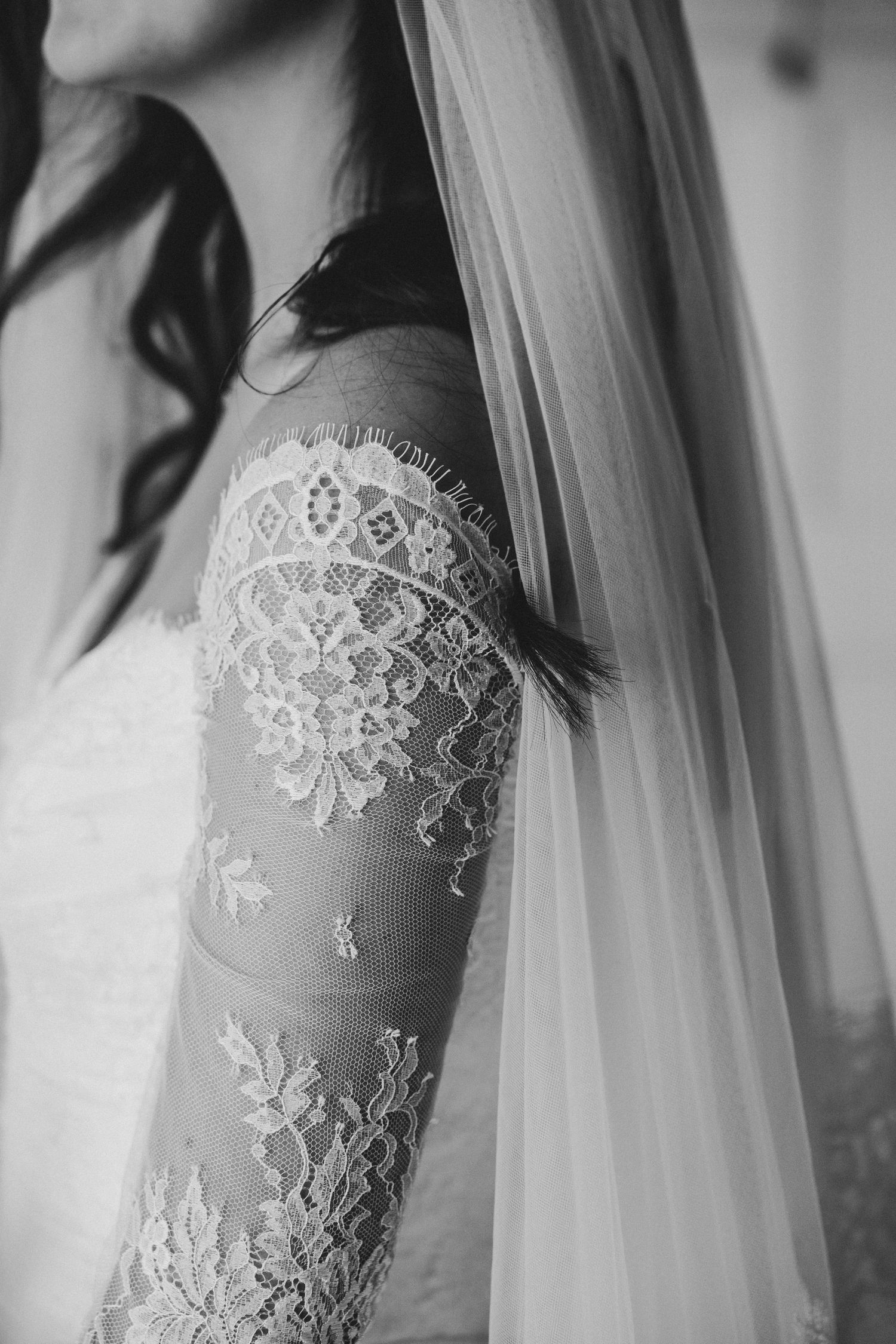 Close-up black and white photo of a bride in a long-sleeve lace wedding gown with delicate floral embroidery and sheer veil.