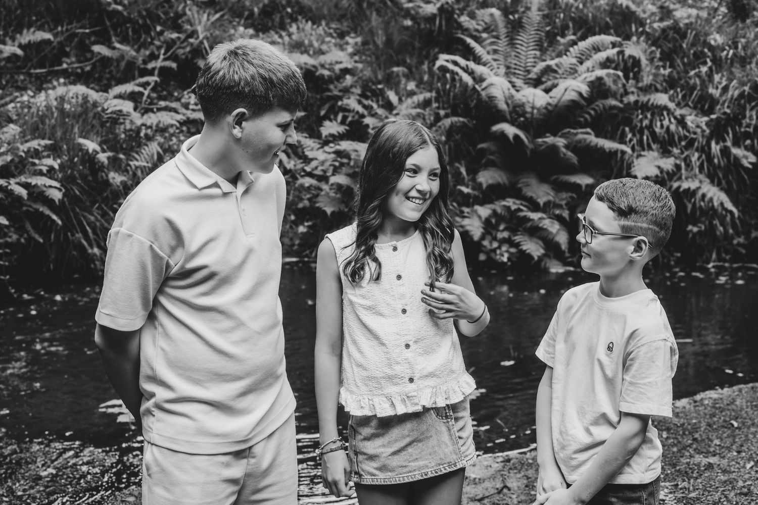 Three children laughing together outdoors in a lush garden, captured in black and white photography.