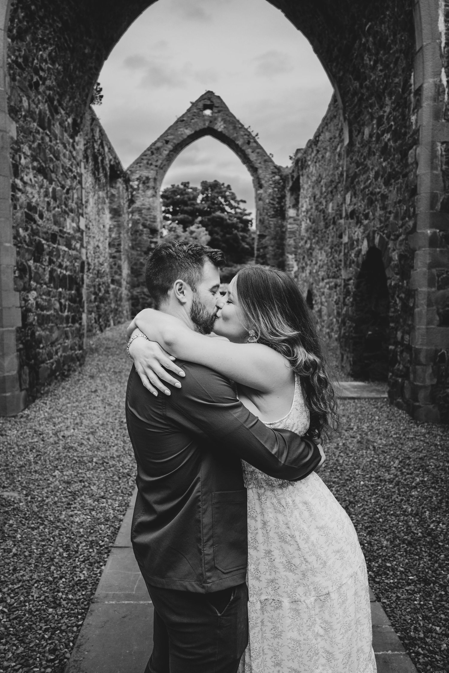 Black and white photo of couple kissing in ancient stone abbey ruins.