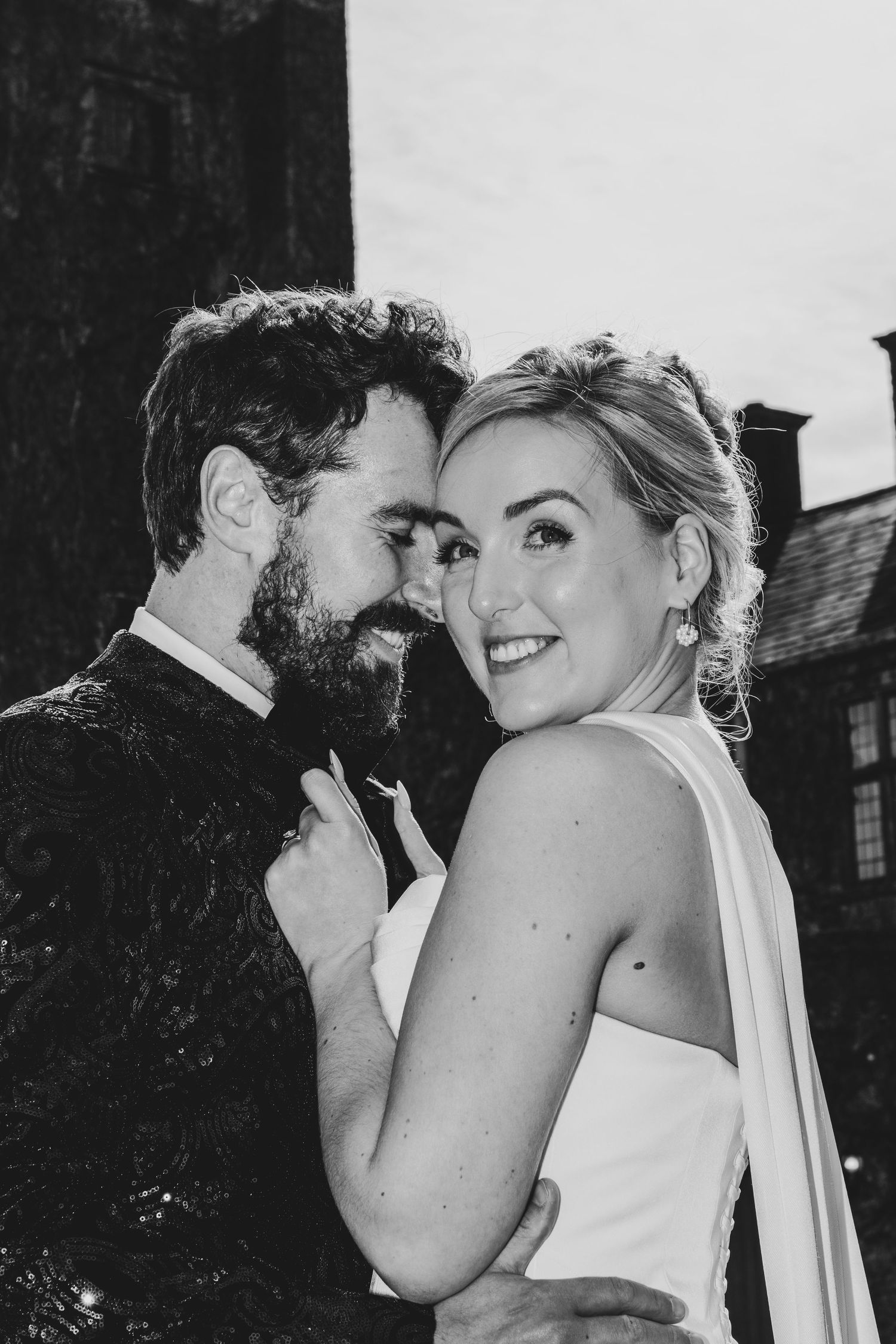 Black and white wedding portrait of smiling bride and bearded groom embracing tenderly outdoors.