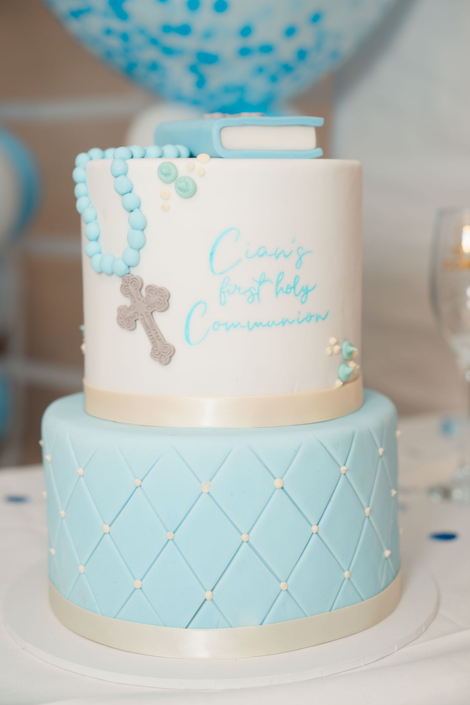 Two-tier white and blue fondant cake for Cian's First Holy Communion, decorated with rosary beads and cross.