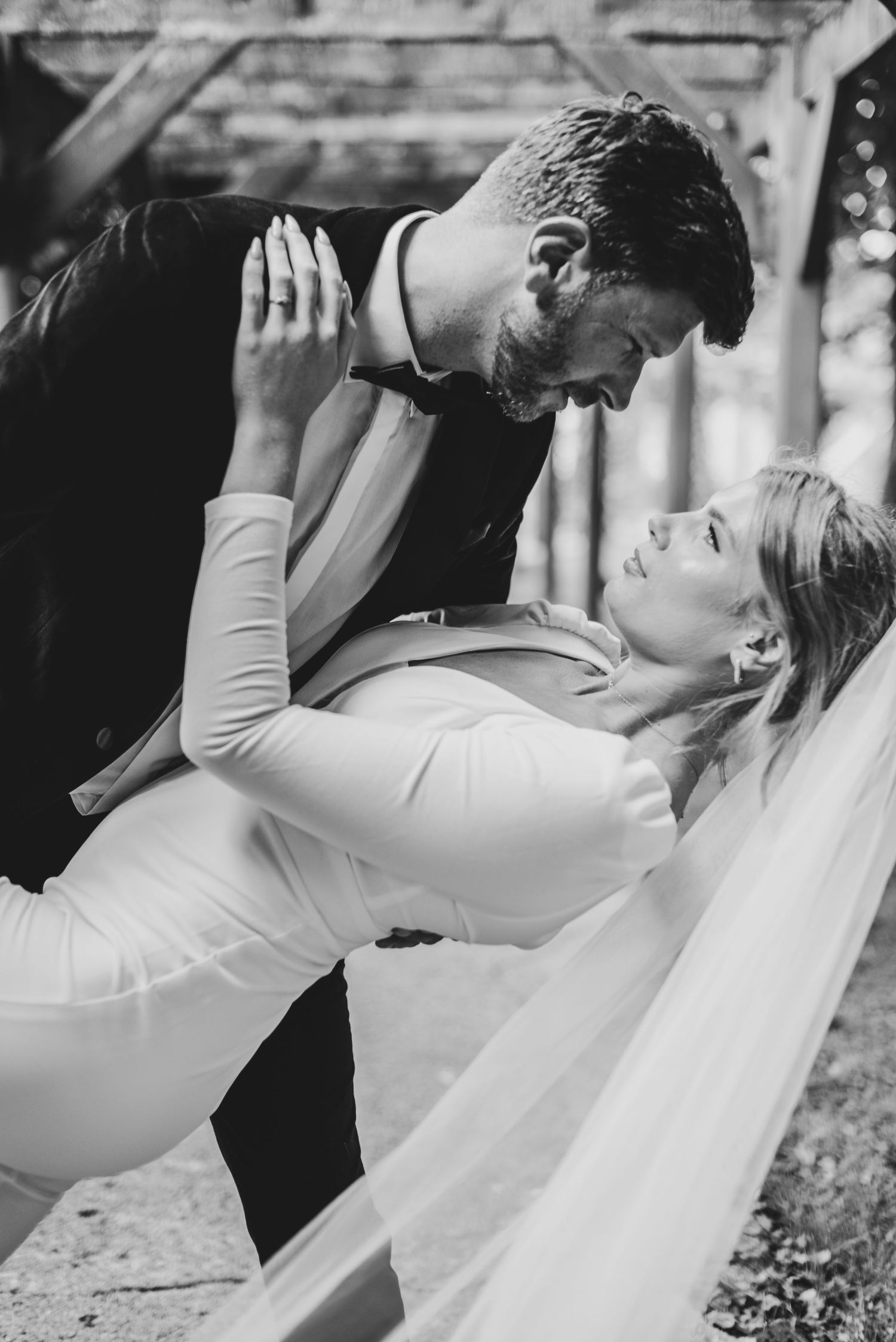 Black and white wedding photo of bride and groom sharing a romantic dip pose outdoors.