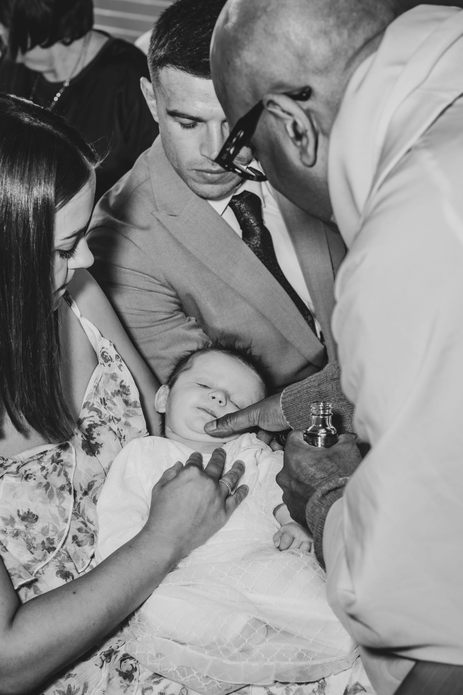 Black and white photo of a baby baptism ceremony with family members gathered around an infant.