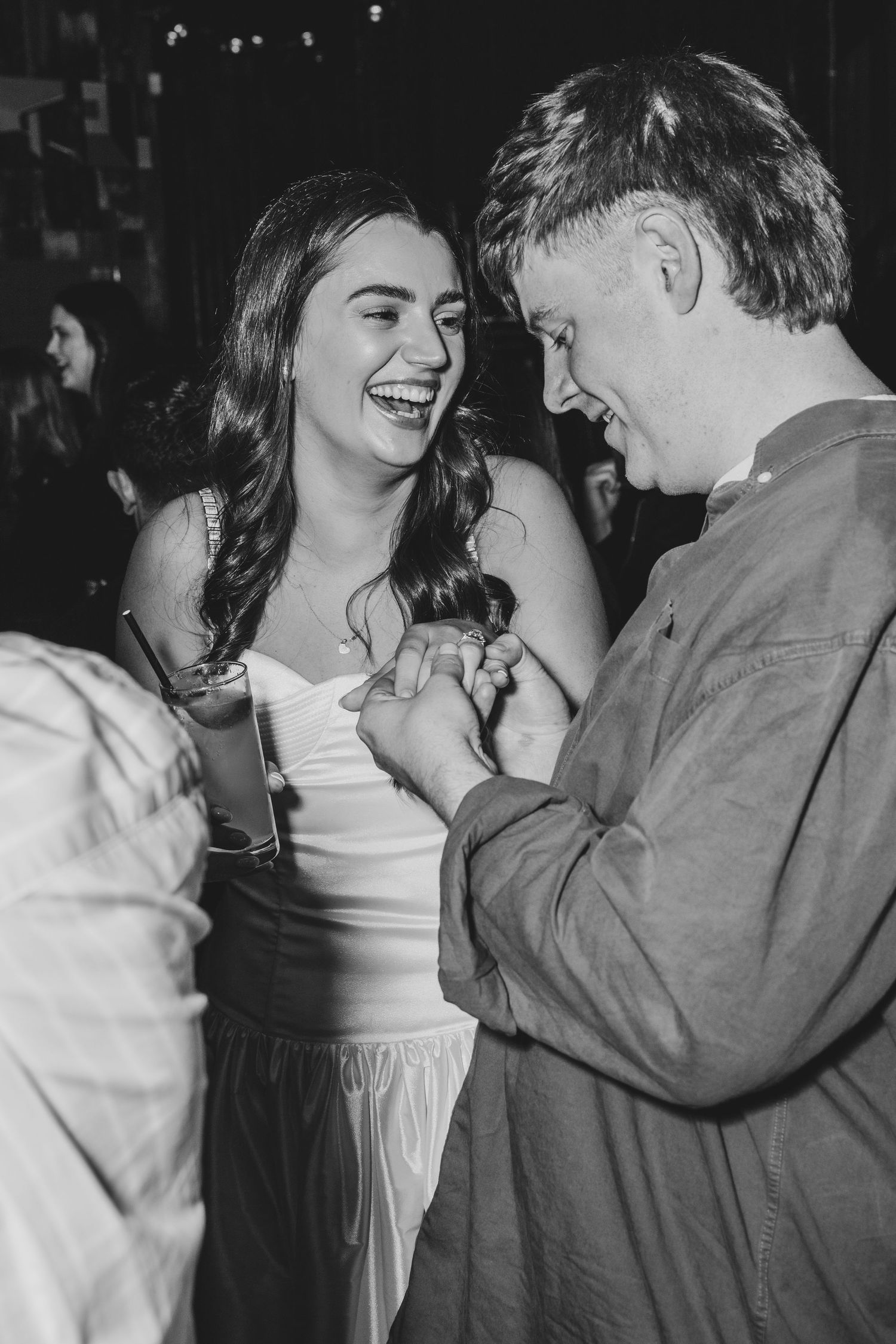 Black and white photo of a laughing couple holding hands and sharing a joyful moment at a social event.