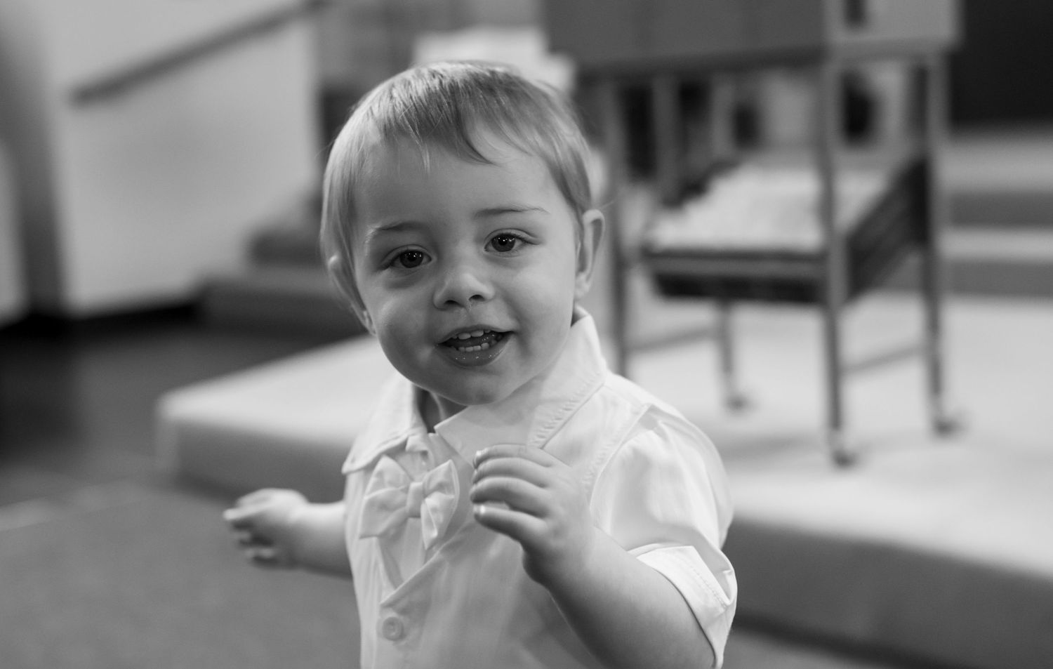 Smiling toddler in white shirt poses playfully in black and white photo.