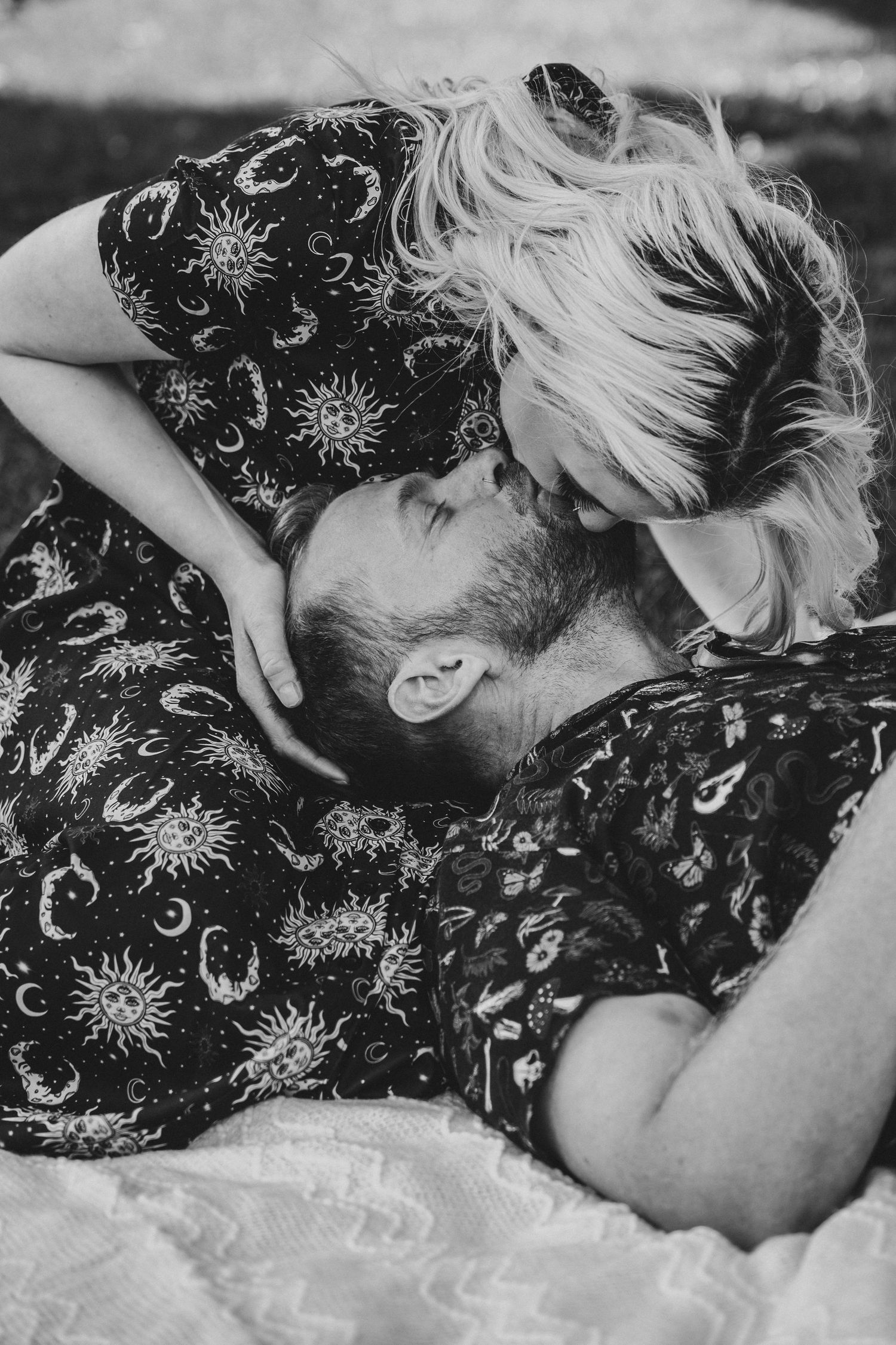 Black and white photo of a couple sharing a tender kiss while lying down outdoors.