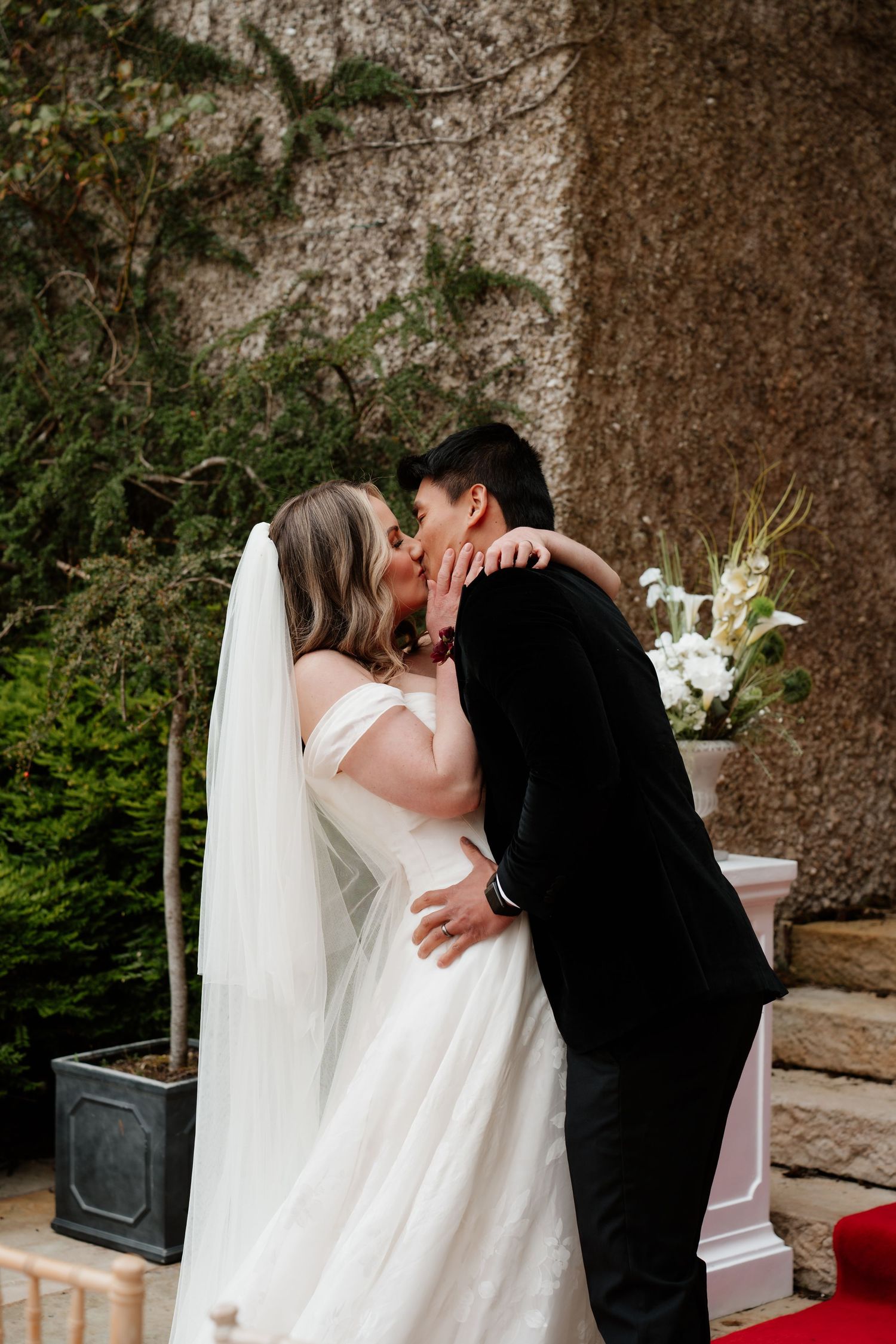 Bride and groom share their first kiss at outdoor wedding ceremony, bride in white gown with veil.