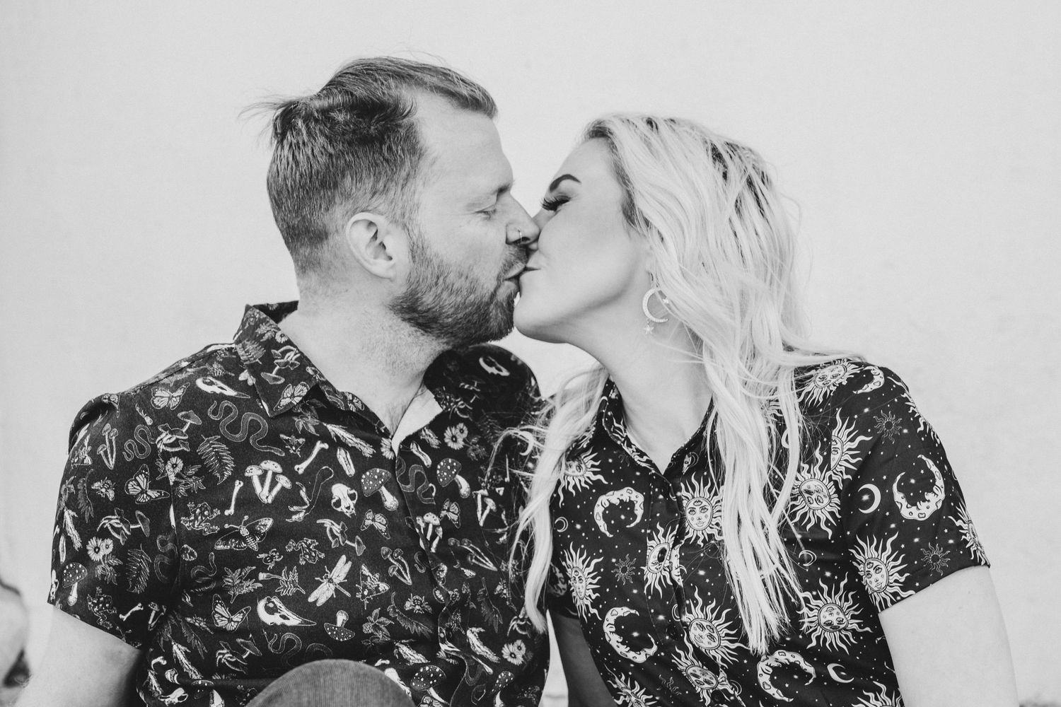 Black and white photo of a couple sharing a romantic kiss, wearing matching patterned shirts.