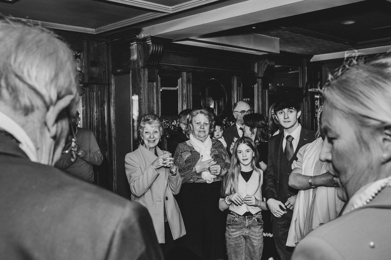 Black and white photo of guests smiling and clapping at an elegant indoor wedding reception event.