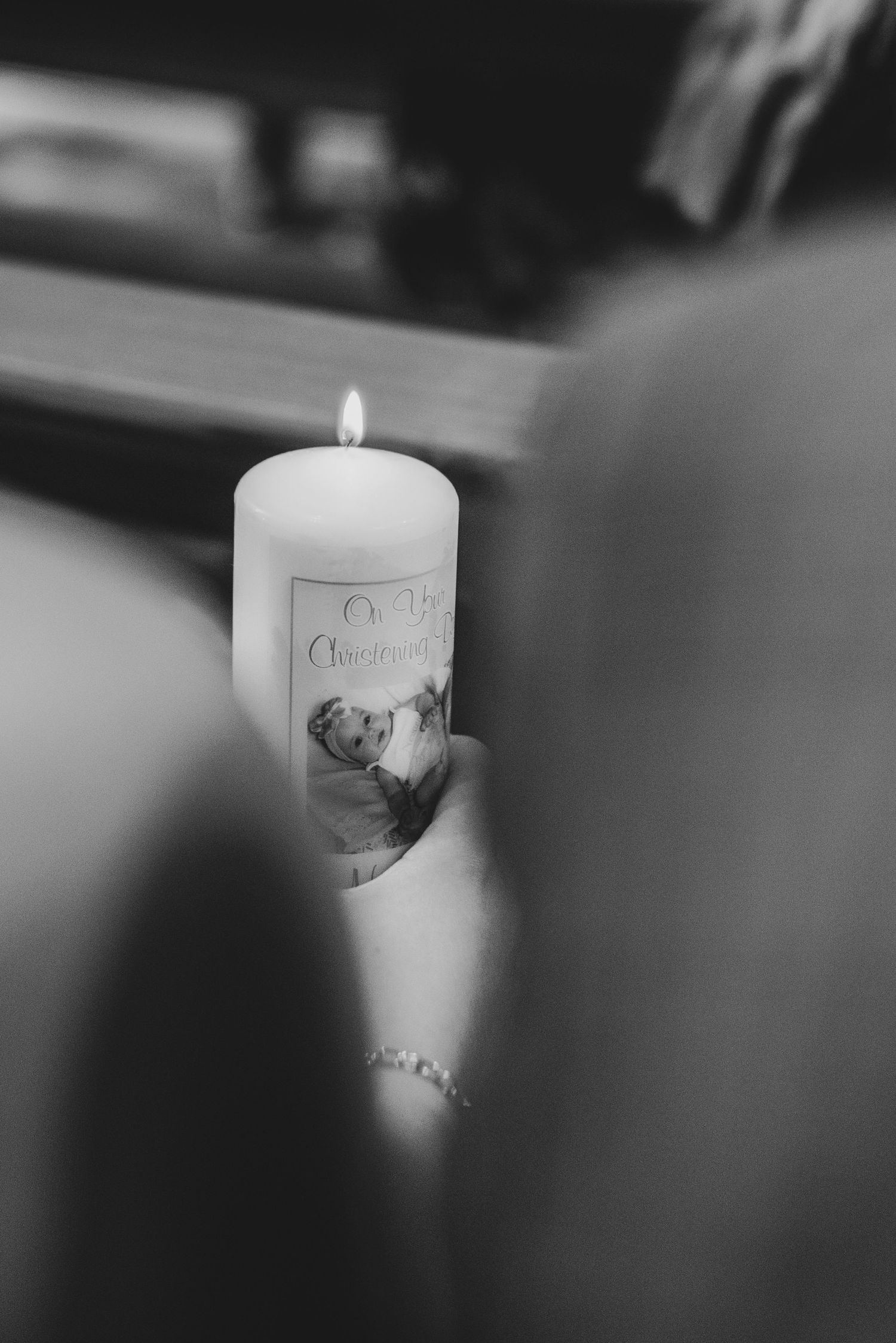 Black and white photo of a lit christening candle with a baby portrait held during a baptism ceremony.
