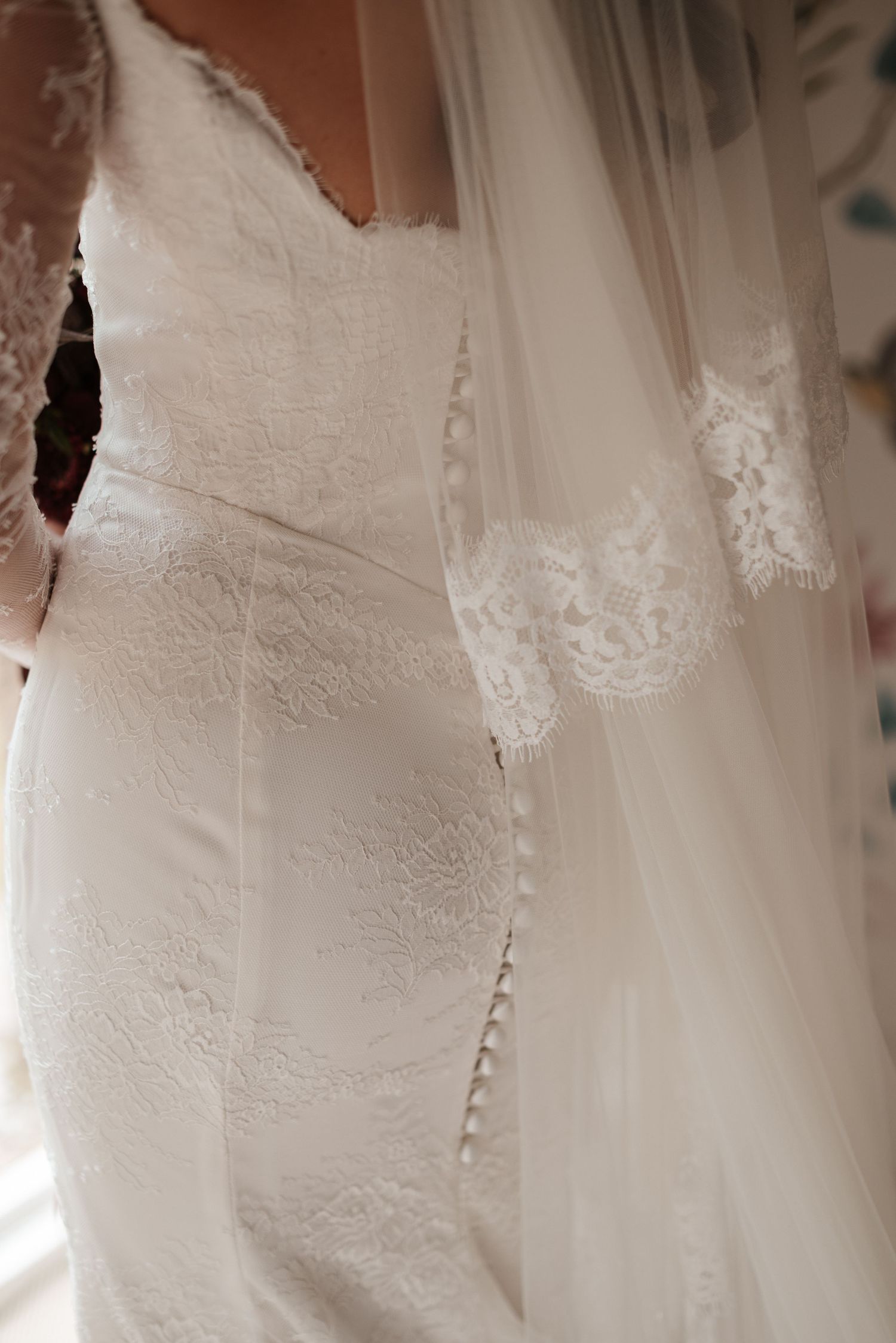 Close-up of an elegant lace wedding dress with button back detail and matching lace-trimmed veil.