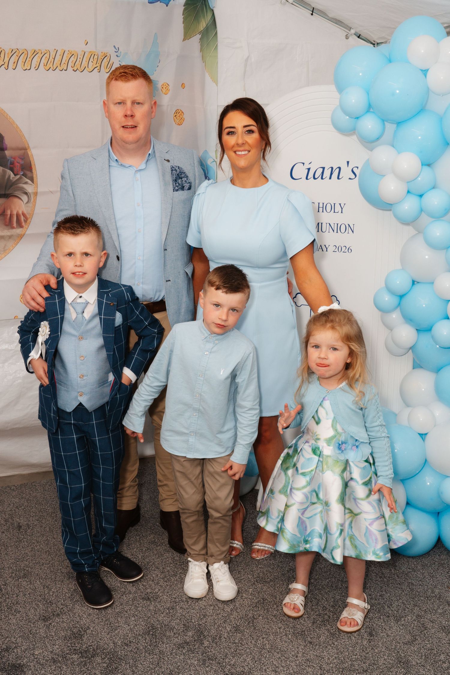Family of five posing at Cian's Holy Communion celebration, decorated with blue balloons and a festive backdrop.