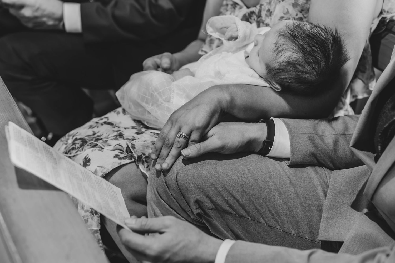 Black and white photo of a newborn baby being held during a baptism ceremony.