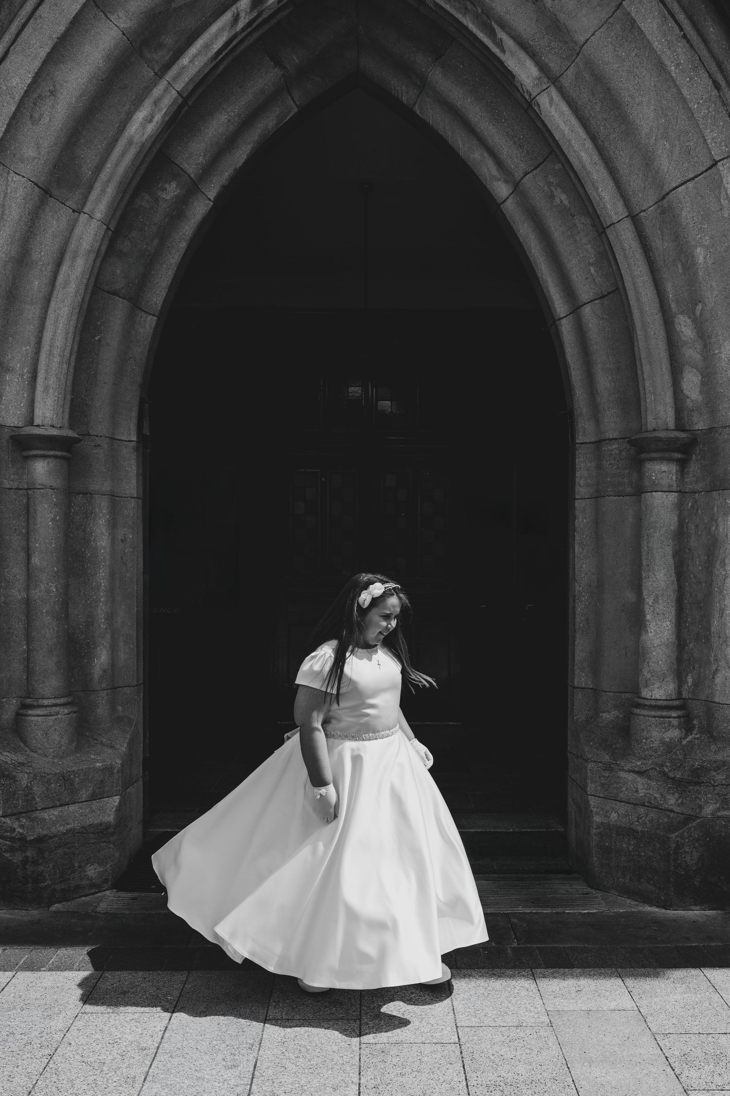 Black and white photo of a bride in a white gown twirling in a Gothic church doorway.