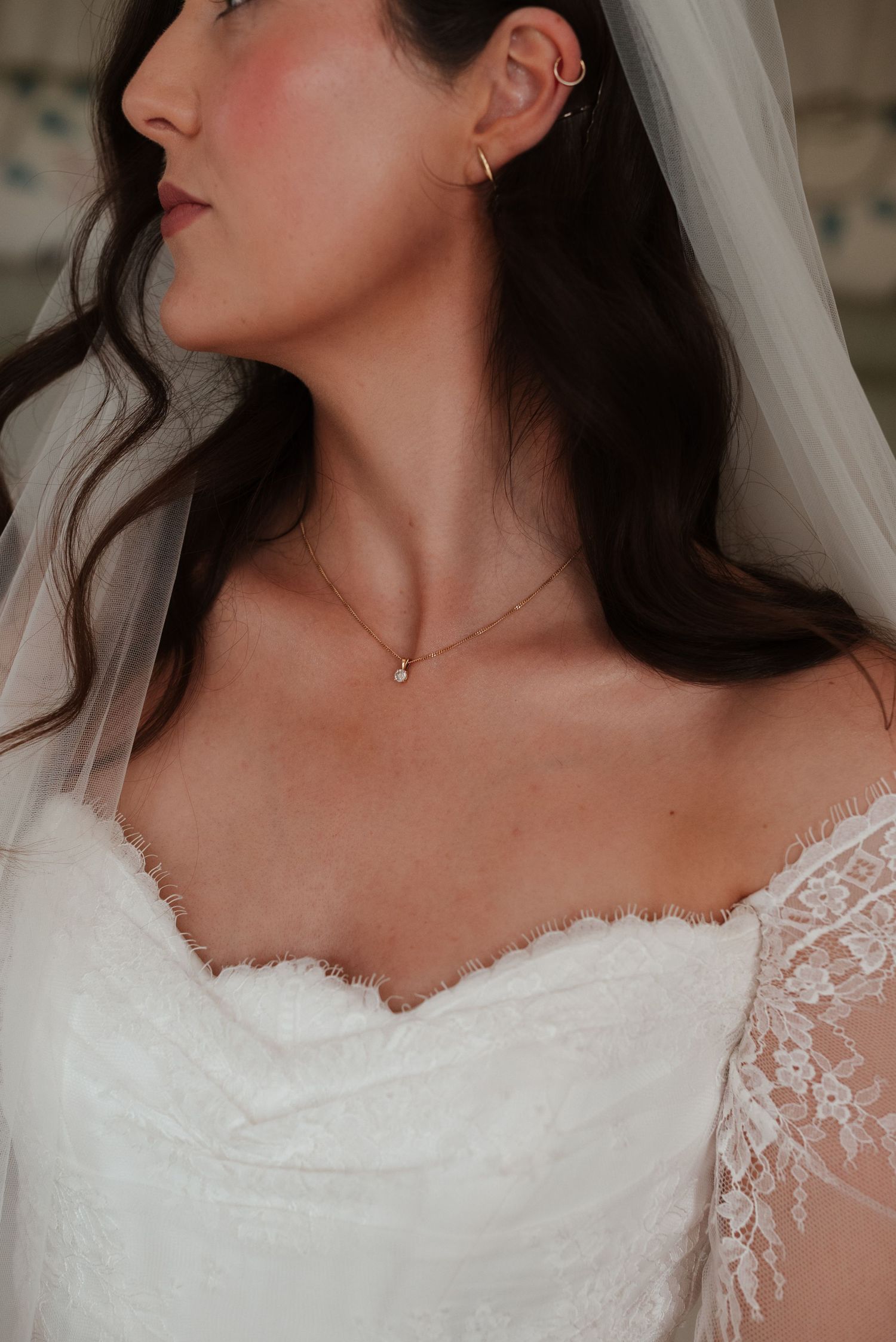 Close-up of bride wearing strapless lace wedding dress with delicate necklace and ear cuff with veil.