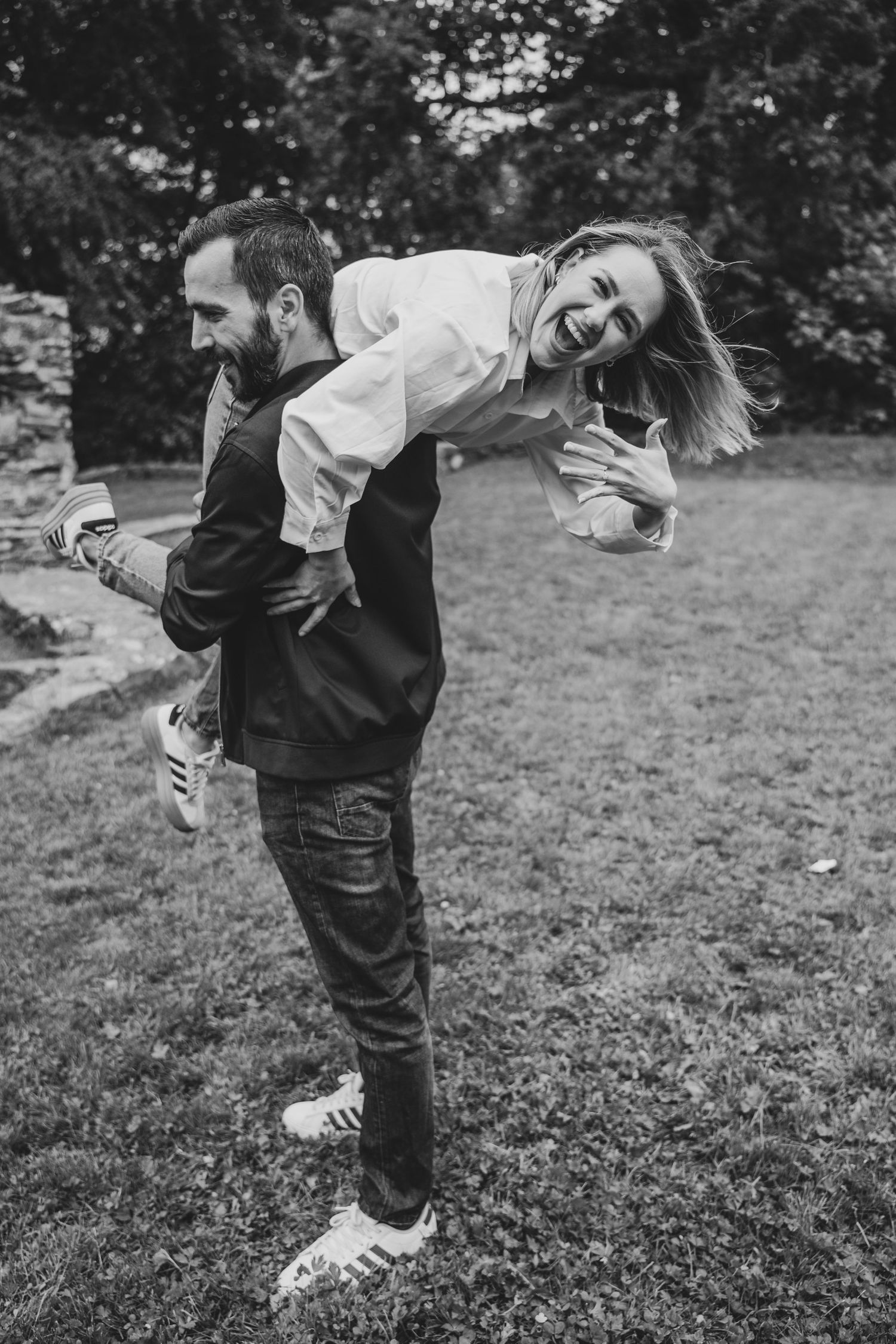 Black and white photo of a man giving a laughing woman a piggyback ride outdoors on a green lawn.