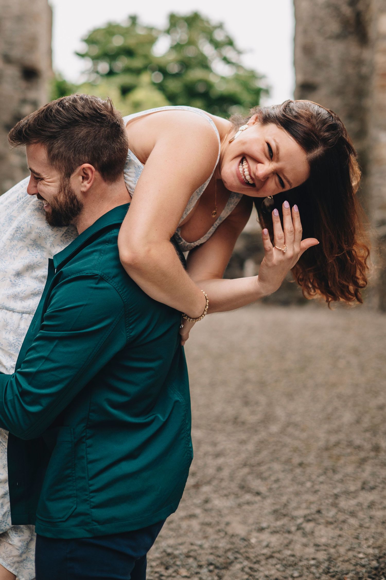 A laughing couple shares a playful piggyback ride outdoors near stone ruins, showing joy and affection.
