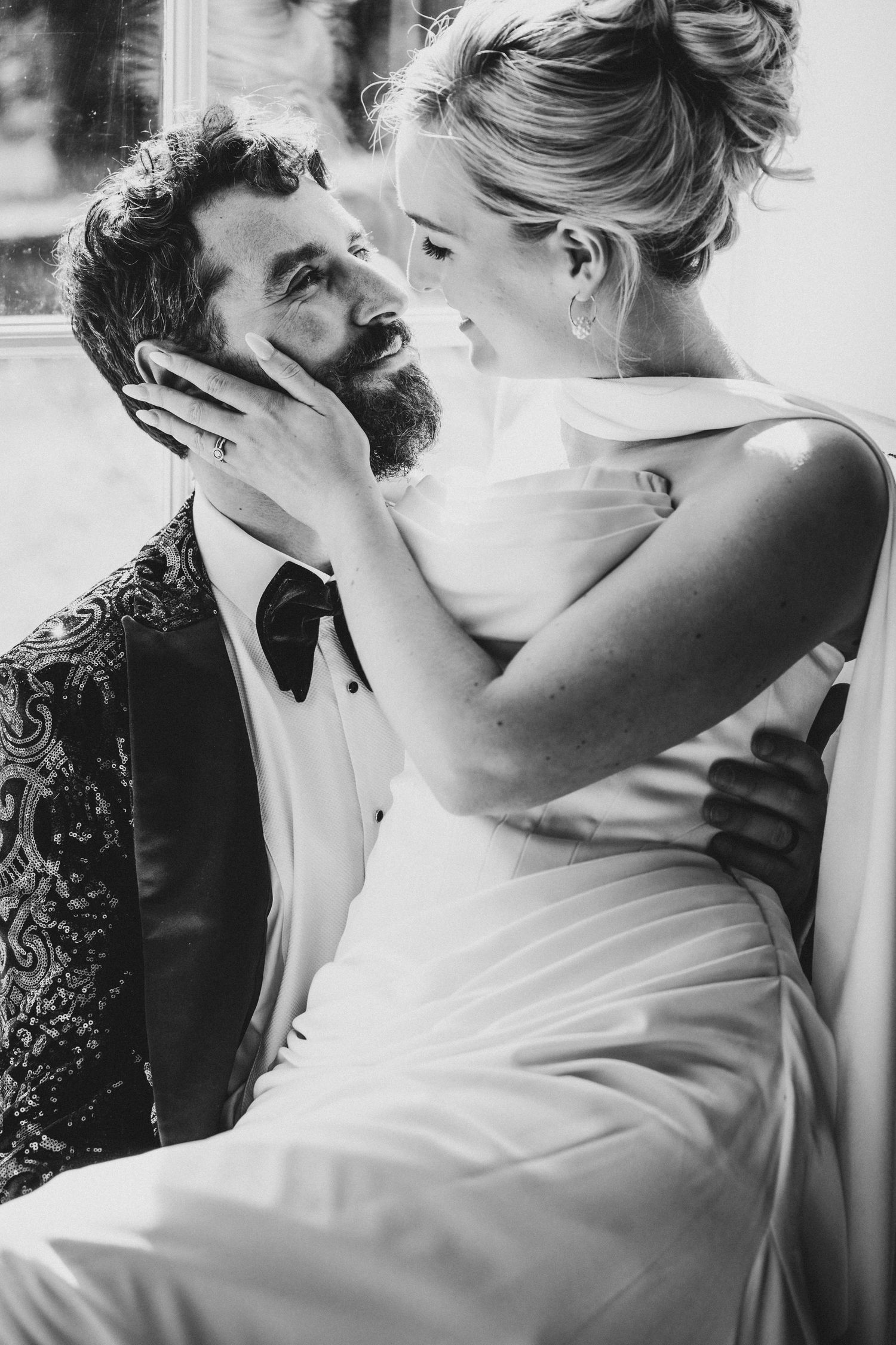 Black and white photo of bride and groom sharing an intimate moment, bride tenderly holding grooms bearded face.