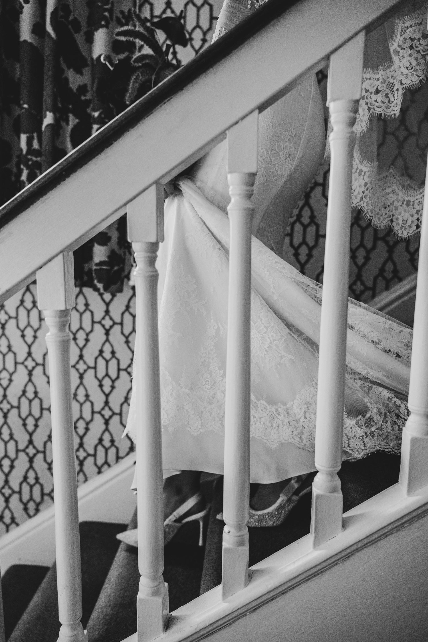 Black and white photo of a lace wedding dress draped over white staircase railings in an elegant home.