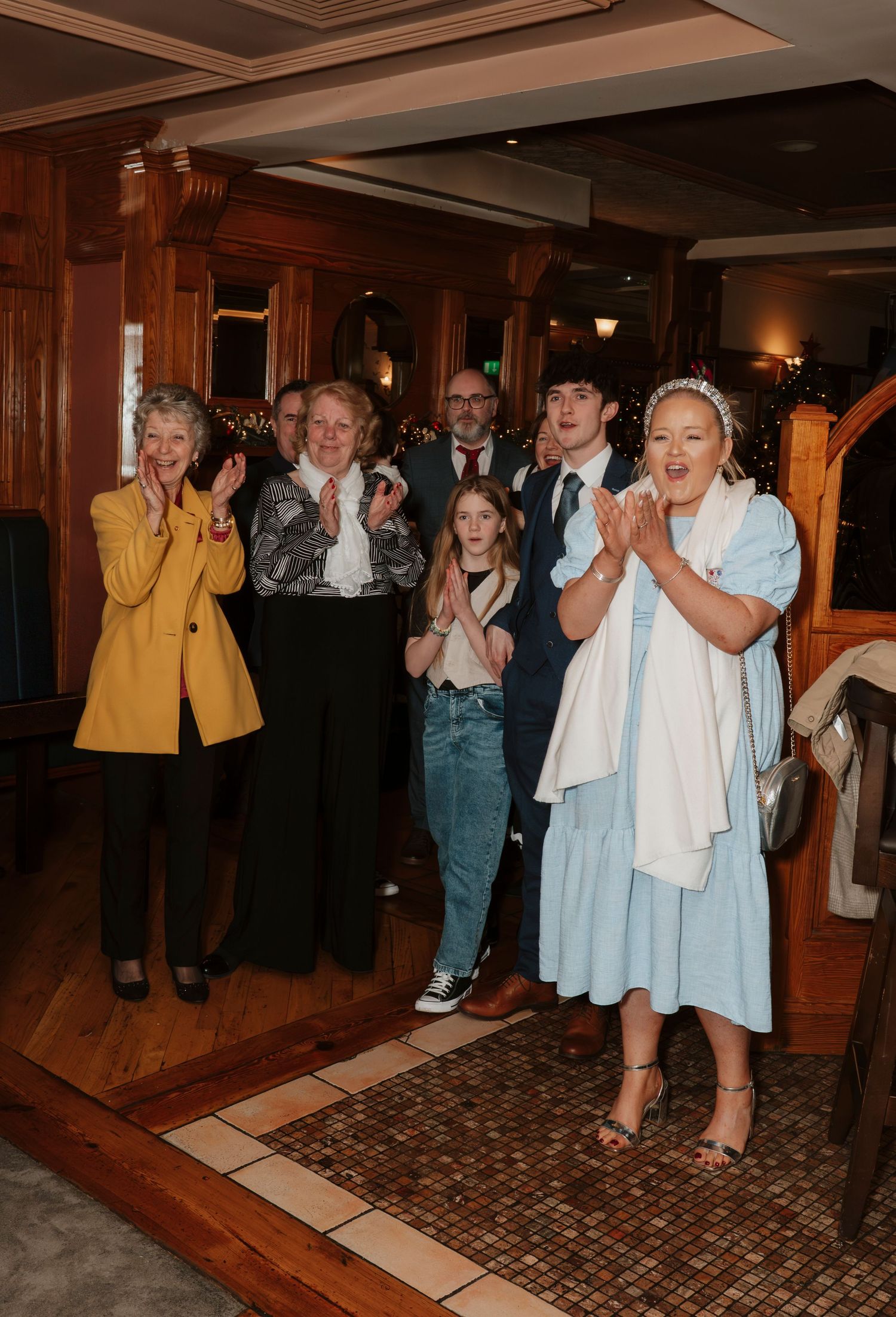 Group of people clapping and celebrating indoors at a restaurant event, dressed in smart casual attire.