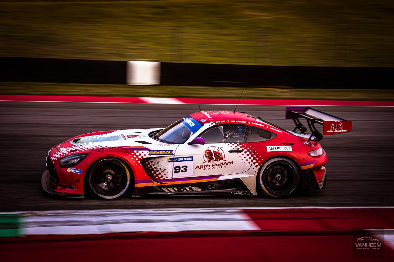 Red racing car speeds along illuminated racetrack at night with motion blur effect showing high-speed action.
