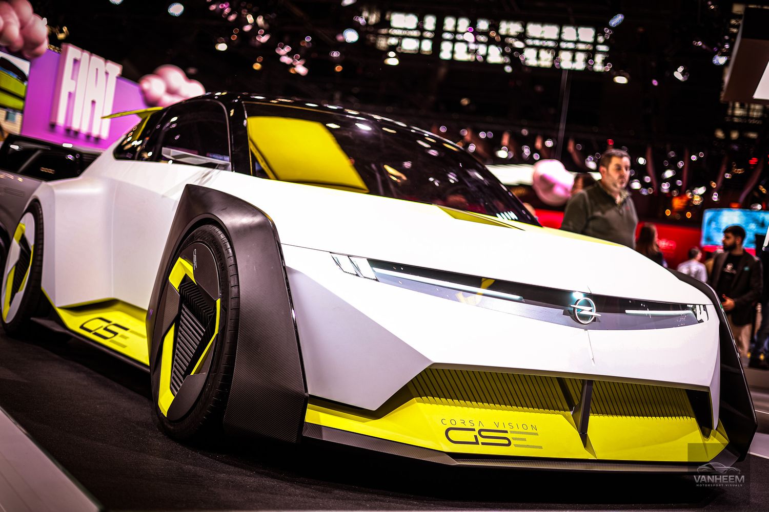 A sleek white and yellow Porsche racing car showcased at an auto show with dramatic lighting effects.